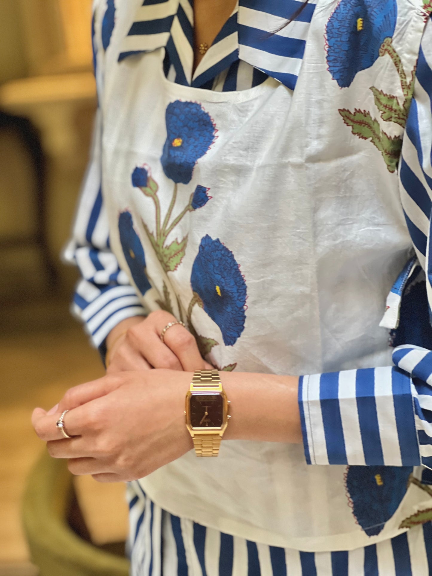 Person wearing a gold watch with a floral apron and striped shirt.