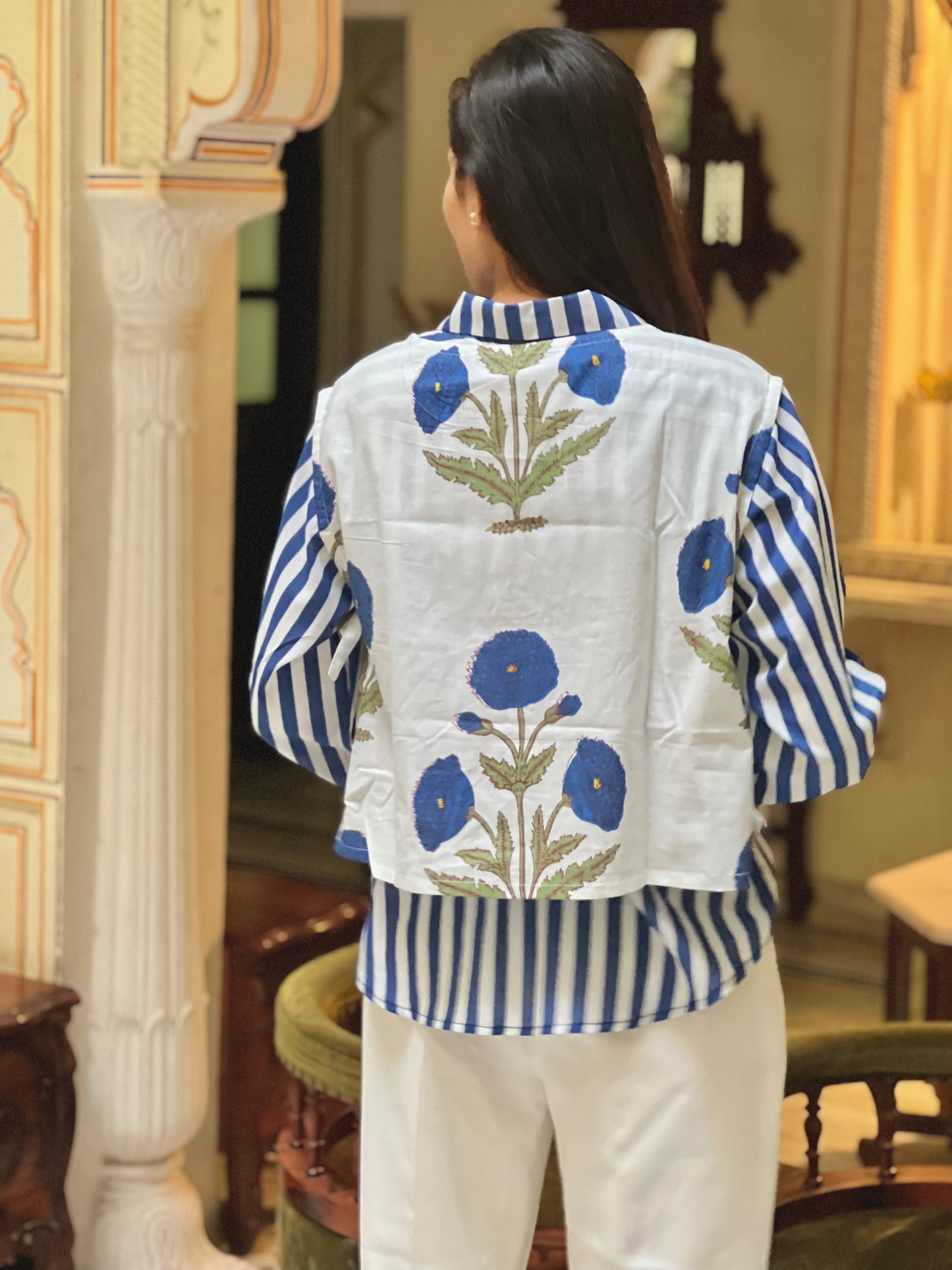 Person wearing a blue and white striped shirt with floral embroidery in a room.