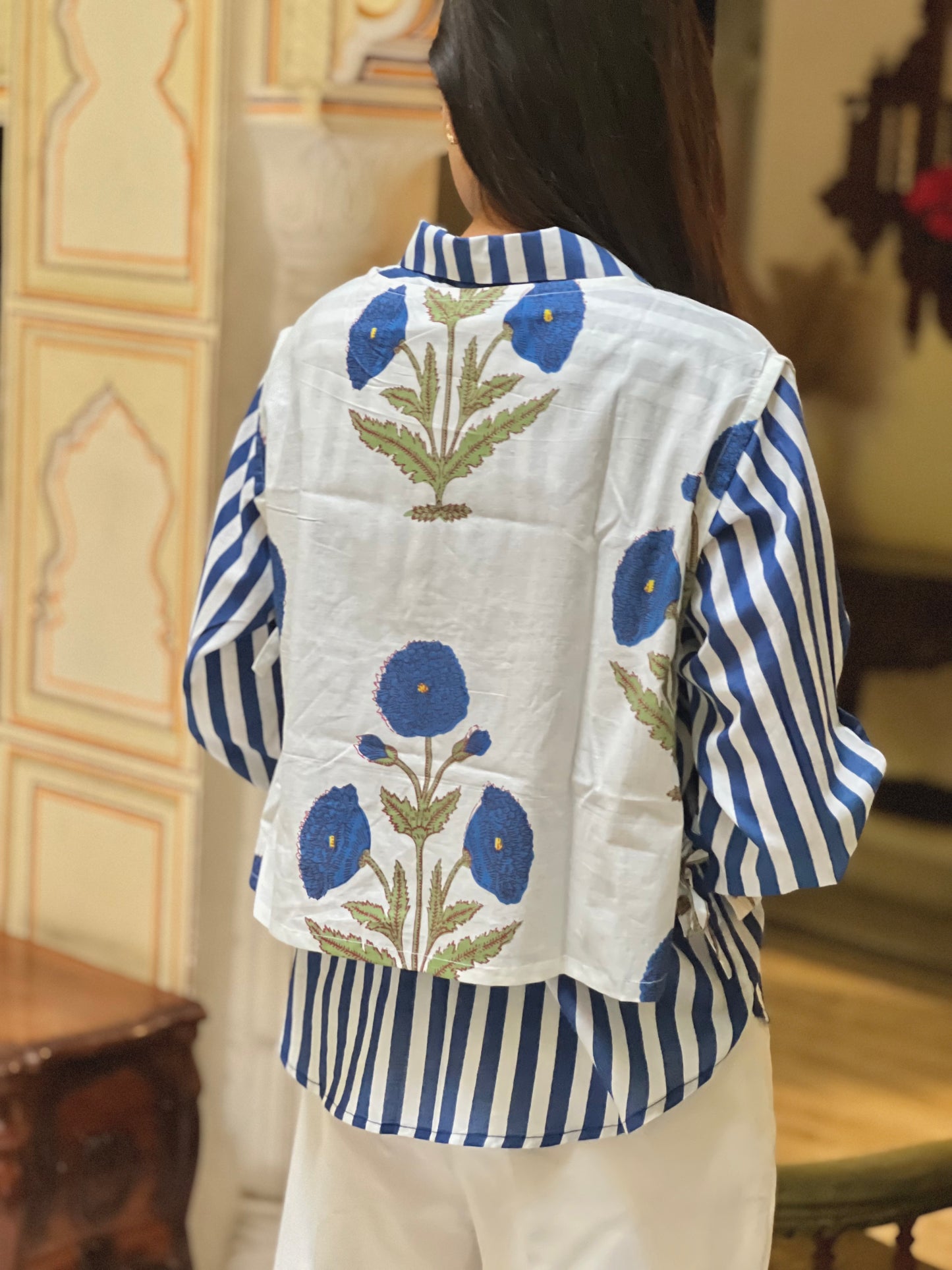 Person wearing a blue and white striped shirt with floral embroidery in a room setting.