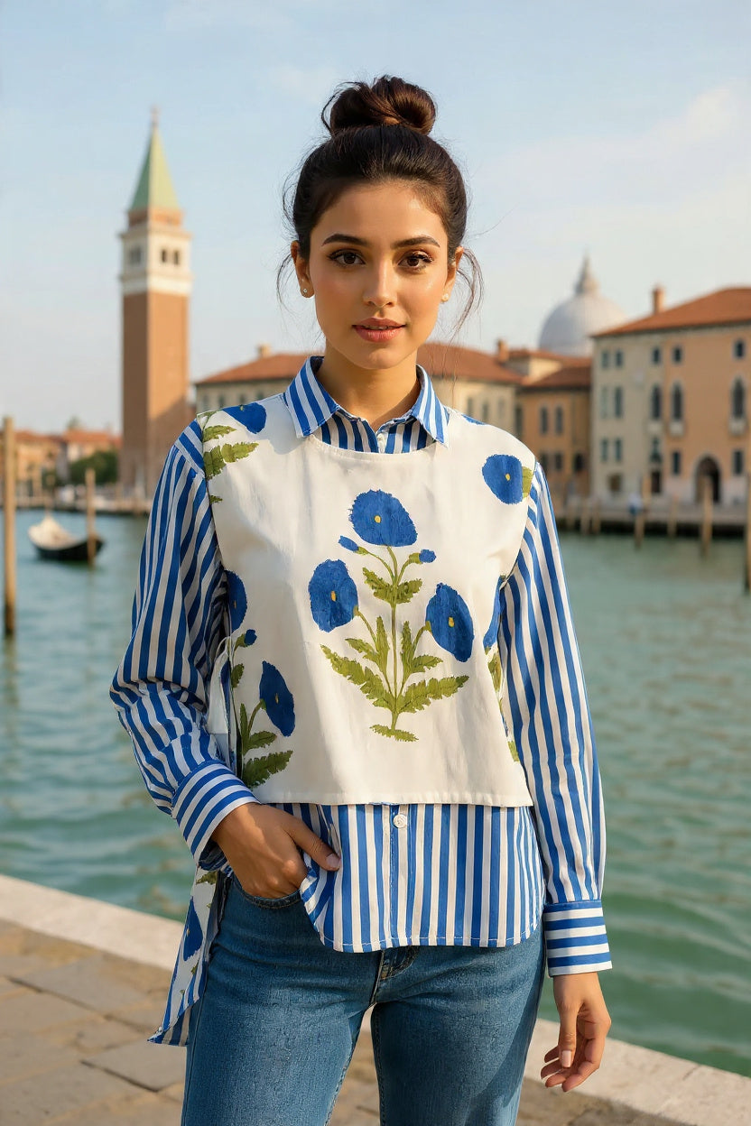 Woman wearing a blue and white striped shirt with a floral apron in front of a waterfront scene.