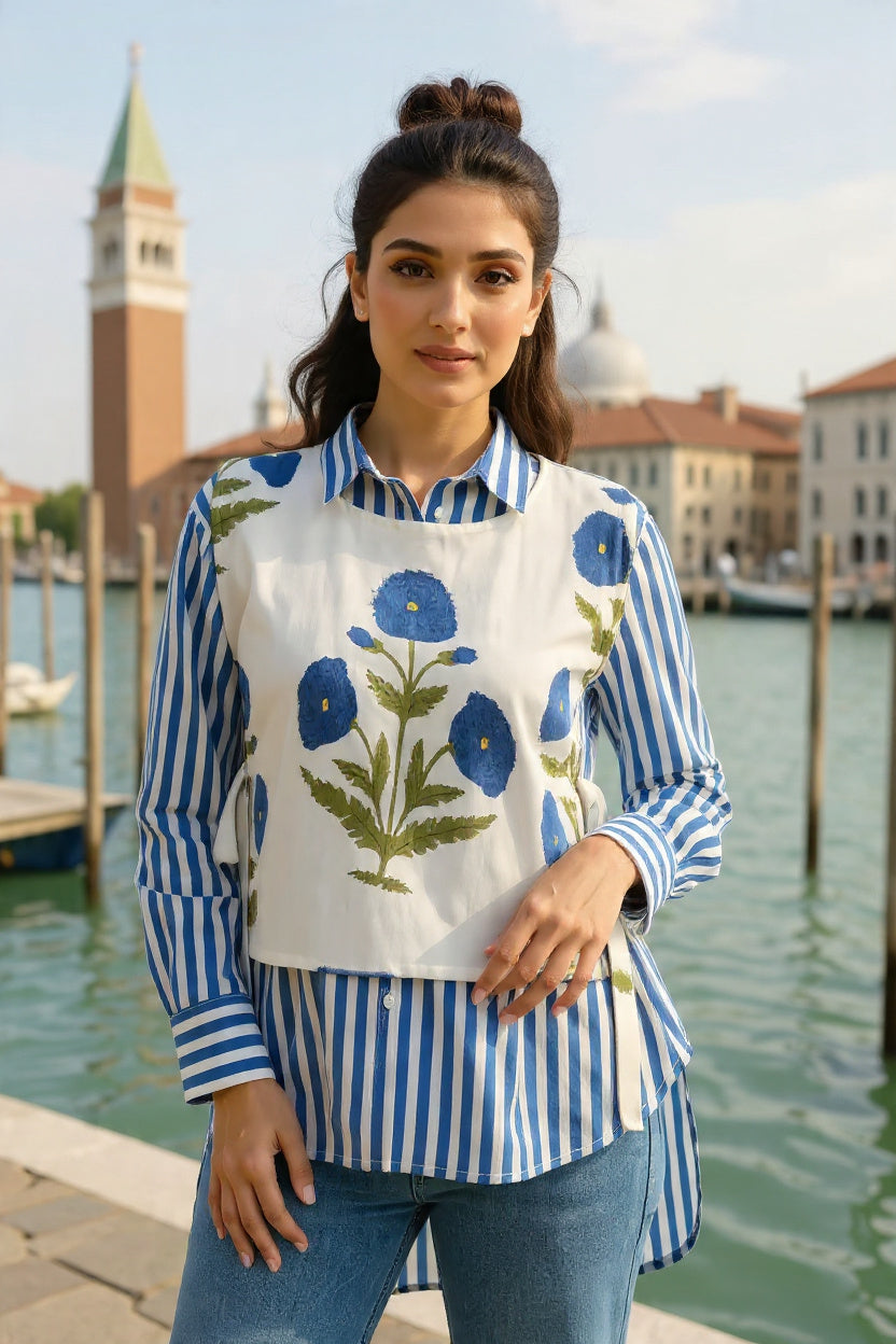 Woman wearing a blue and white striped shirt with a floral apron by a waterfront in an Italian town.