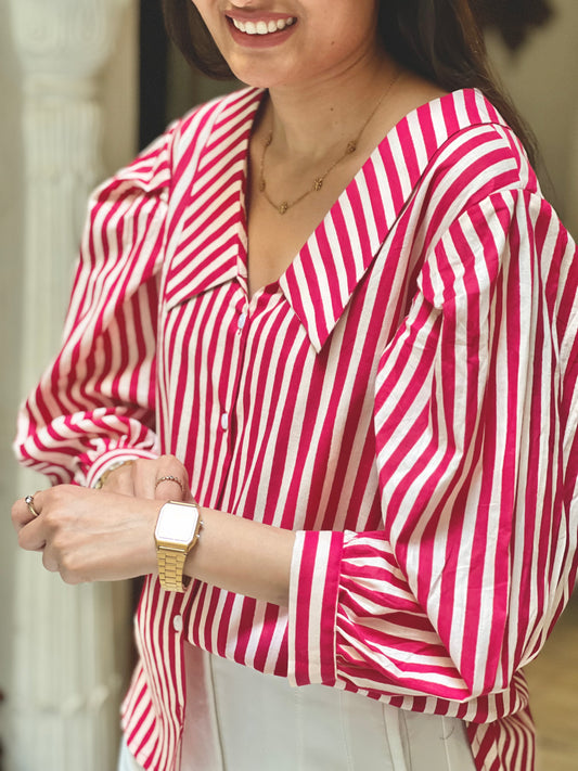 Person wearing a red and white striped shirt with a gold watch, blurred background