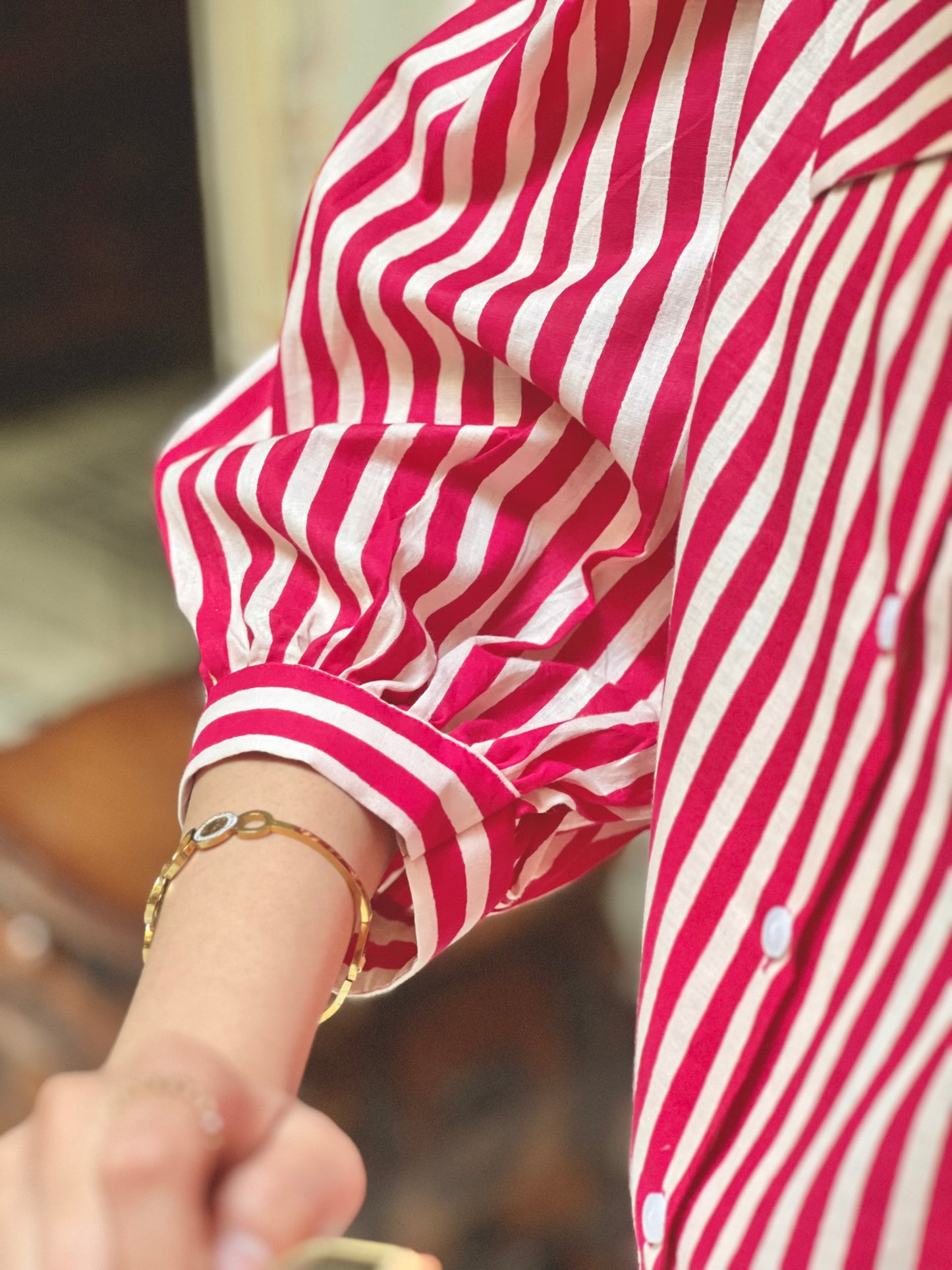Close-up of a person wearing a red and white striped shirt with rolled-up sleeves and a gold bracelet.