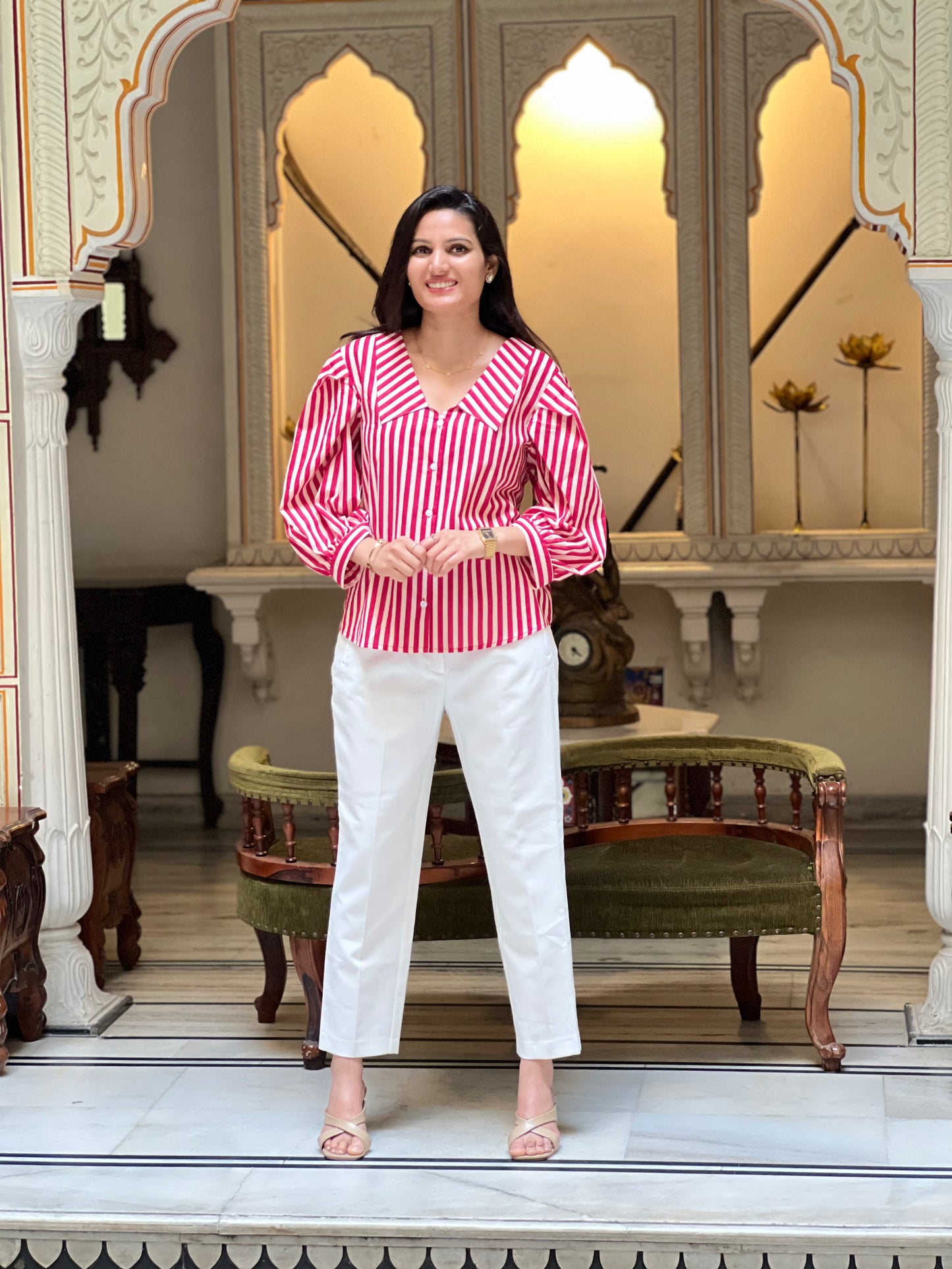 Woman in a red and white striped shirt and white pants standing in an ornate room.