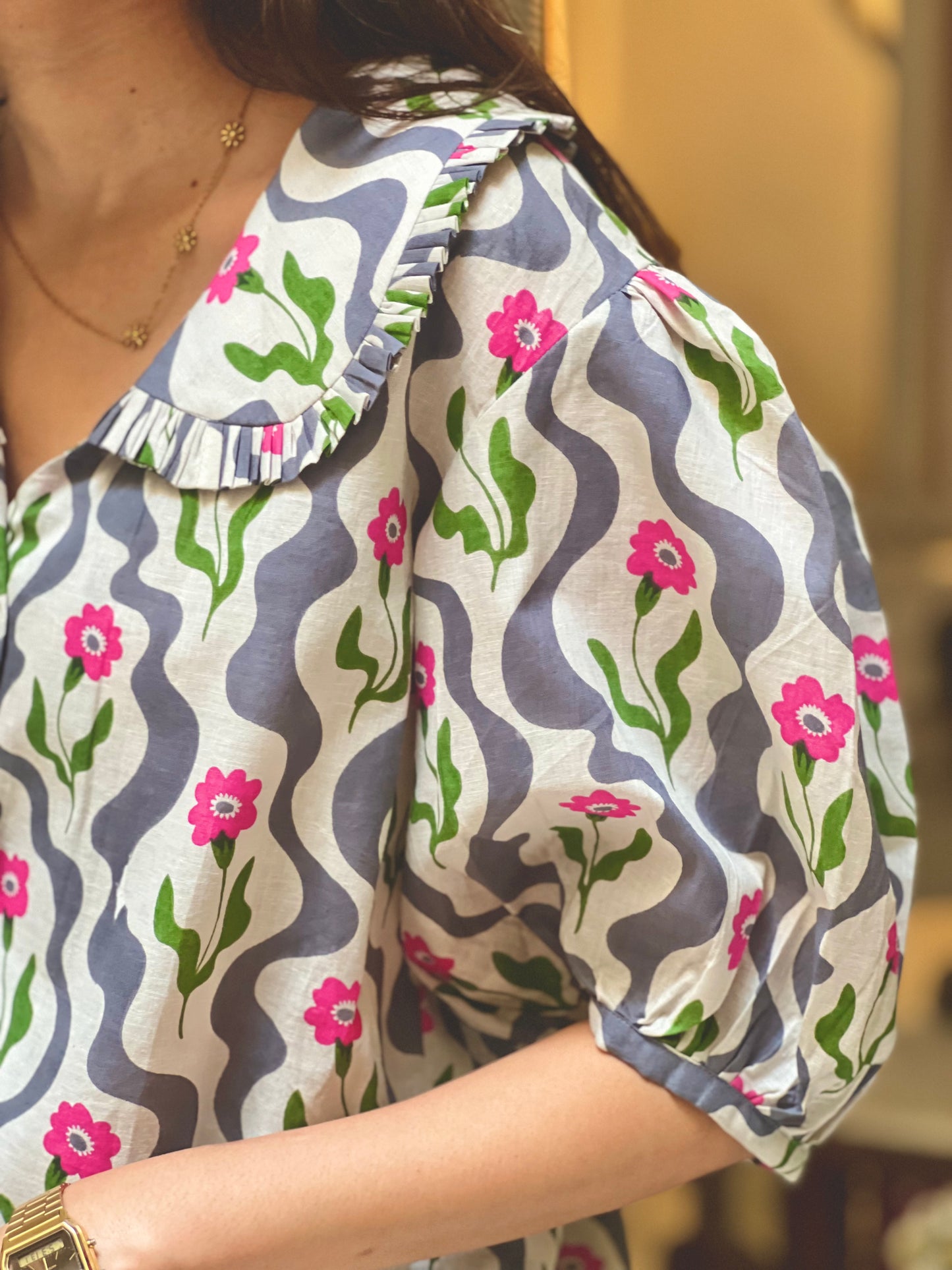 Woman wearing a patterned blouse with floral designs and wavy lines.