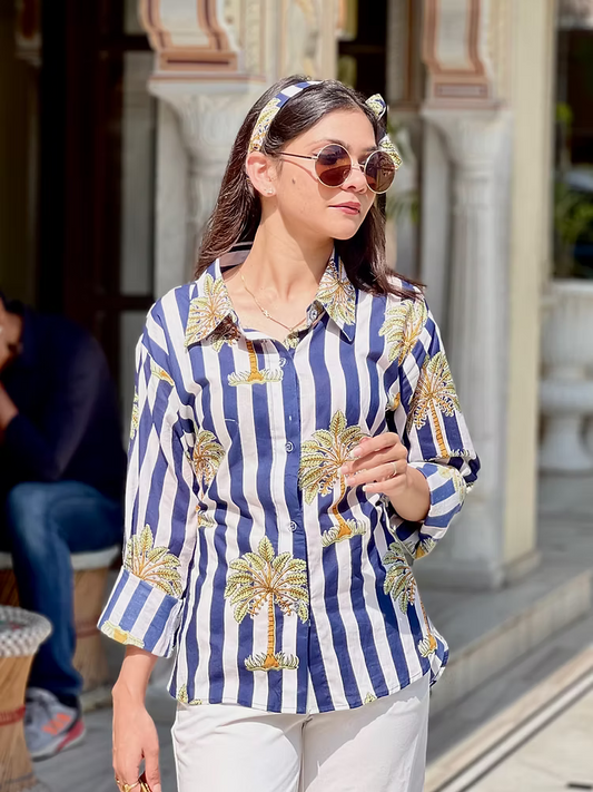 Woman wearing a blue and white striped shirt with palm tree patterns outdoors.