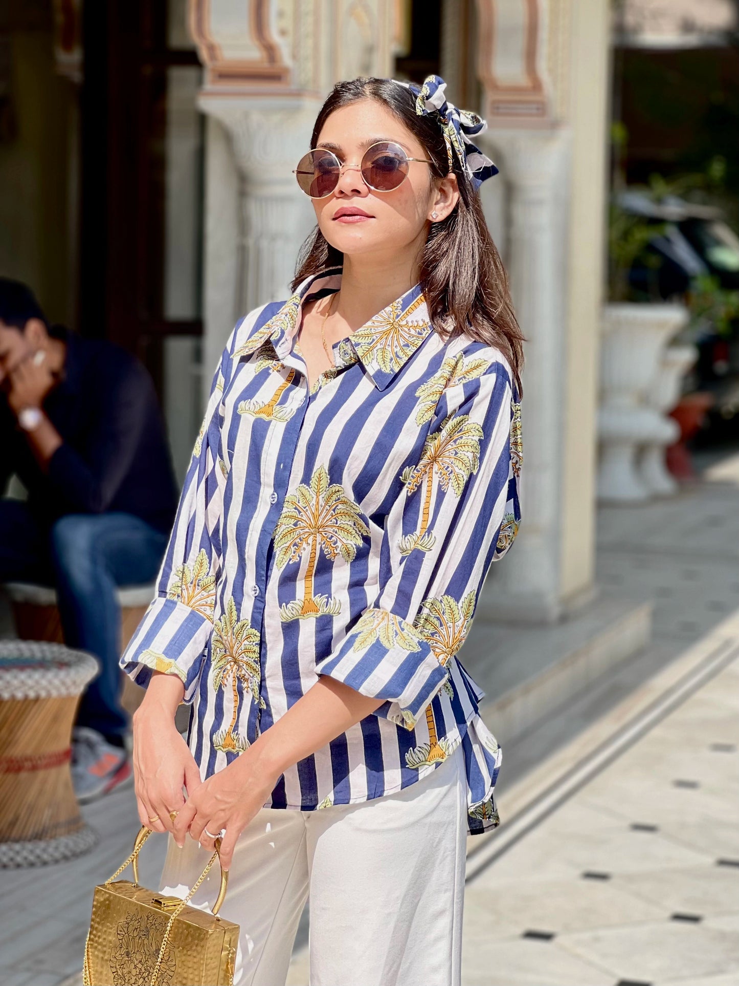 Woman wearing a blue and white striped shirt with palm tree designs outdoors.