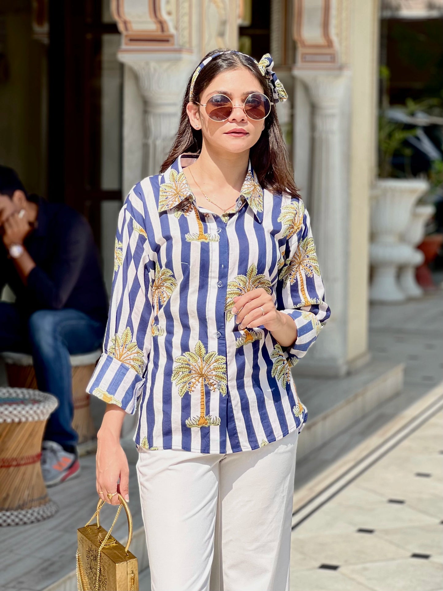 Woman wearing a blue and white striped shirt with palm tree patterns outdoors.