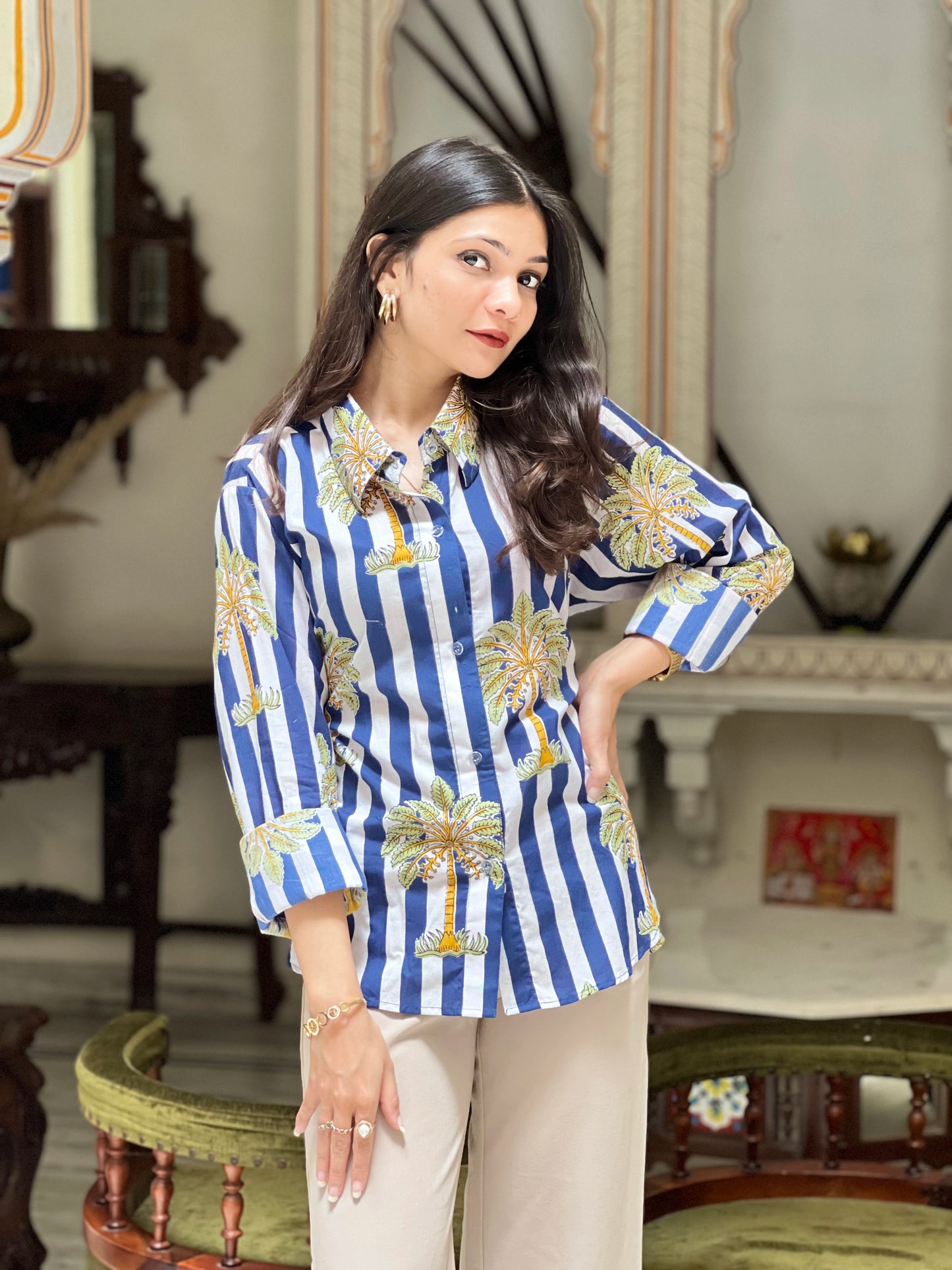 Woman wearing a blue and white striped shirt with floral patterns in an elegant indoor setting.
