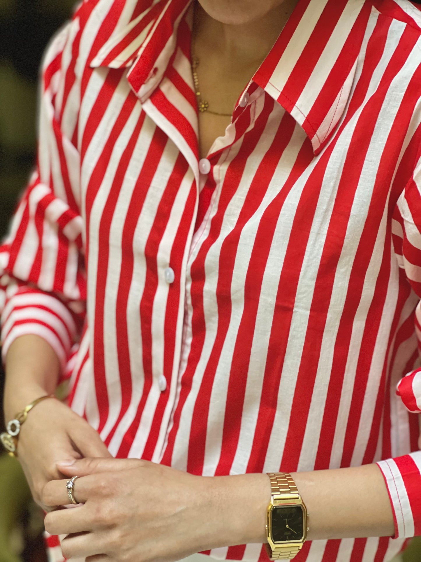 Person wearing a red and white striped shirt with a gold watch on a blurred background