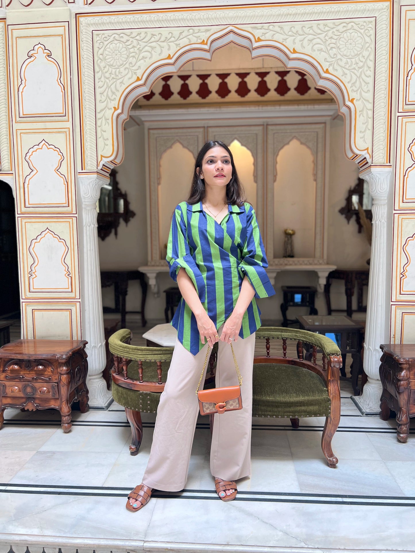 Woman in a striped shirt and beige pants standing in an ornate room with decorative walls and furniture.