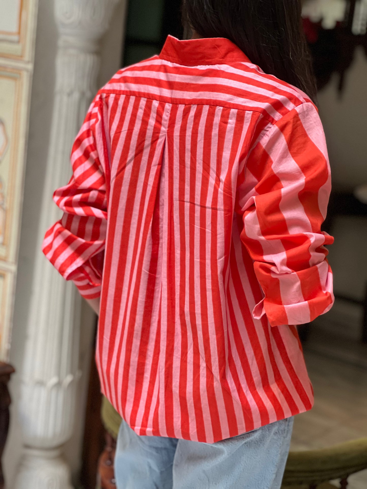 Person wearing a red and white striped shirt with rolled-up sleeves indoors.