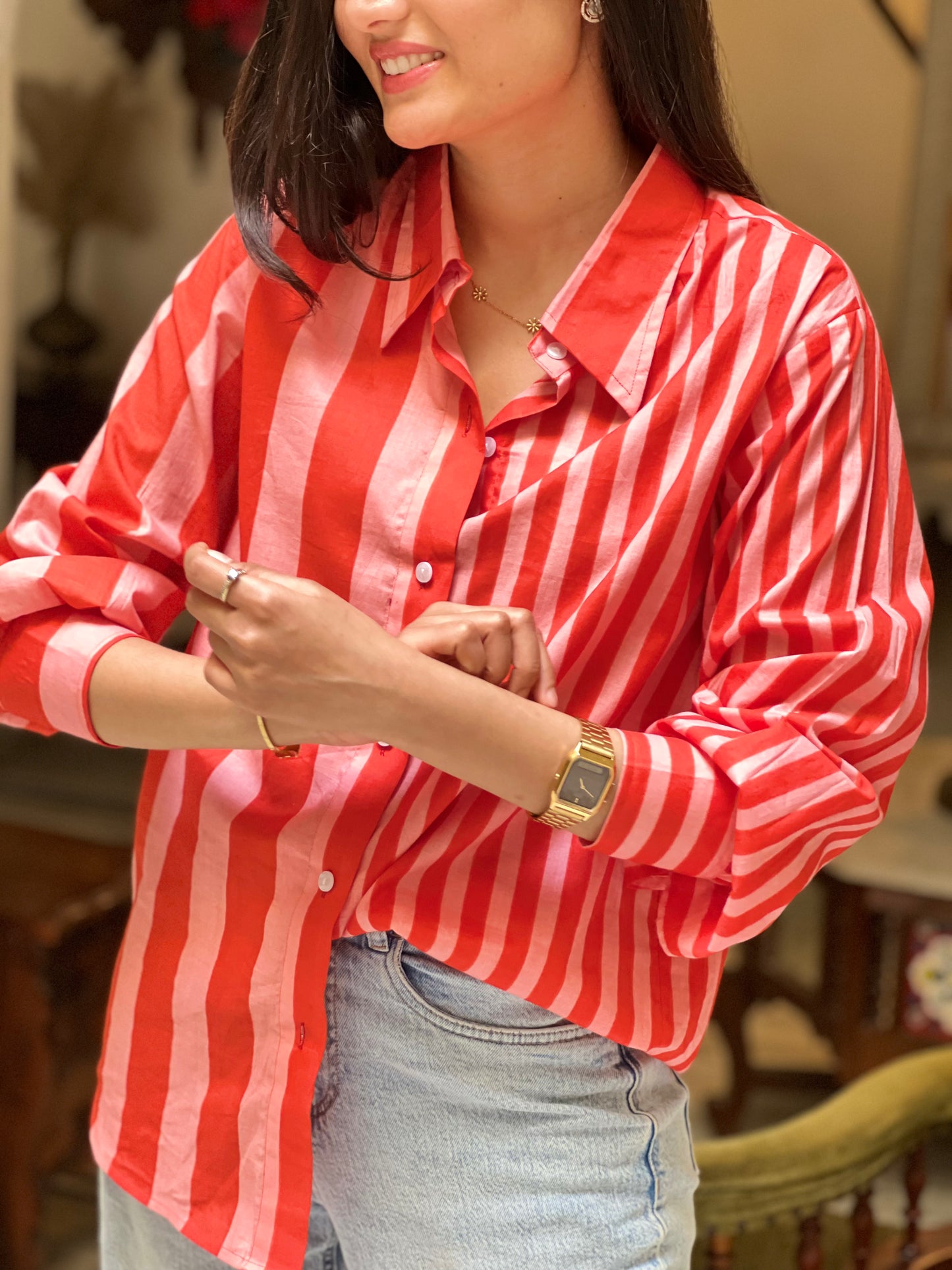 Woman wearing a red and white striped shirt with rolled-up sleeves, standing indoors.