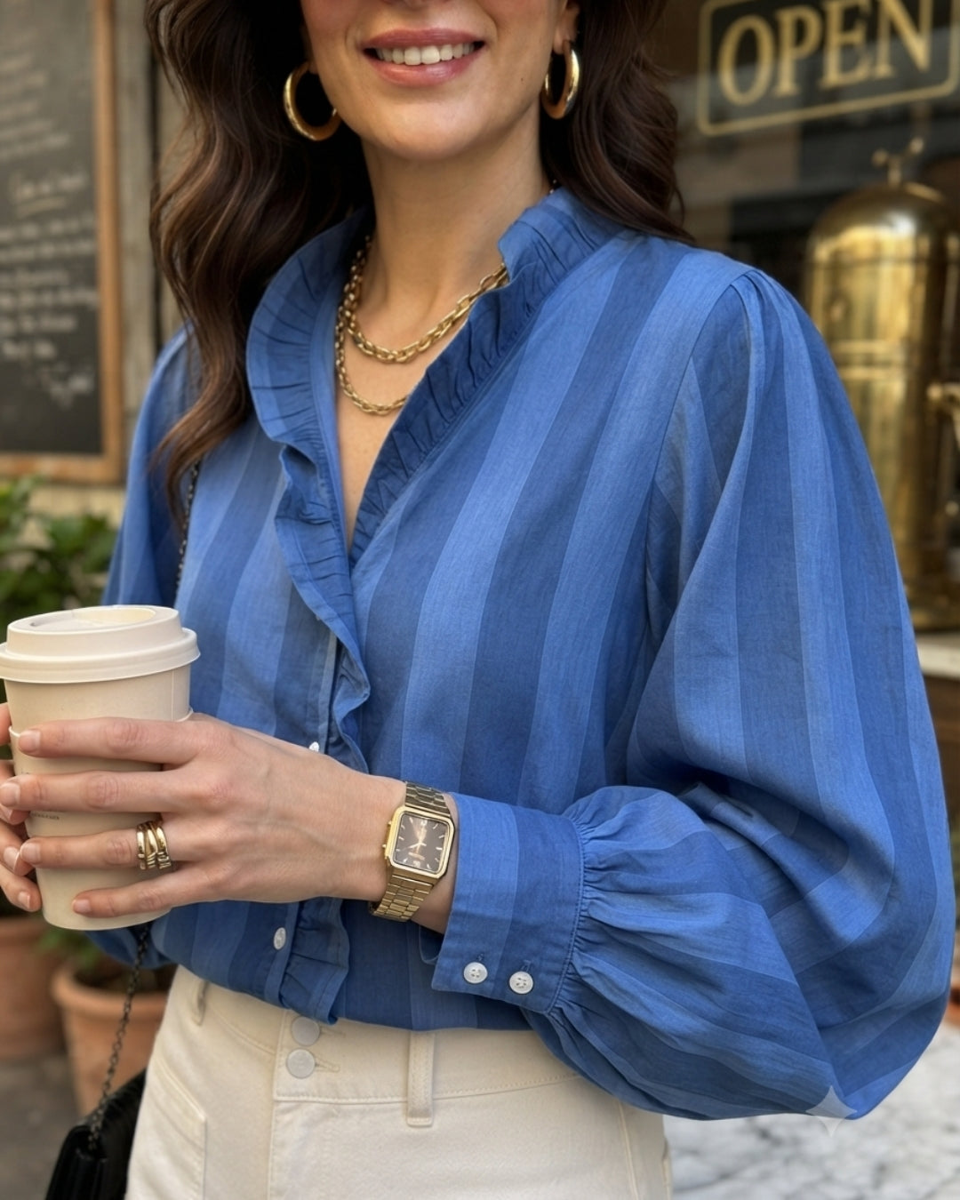 Woman in a blue striped shirt holding a coffee cup outdoors.
