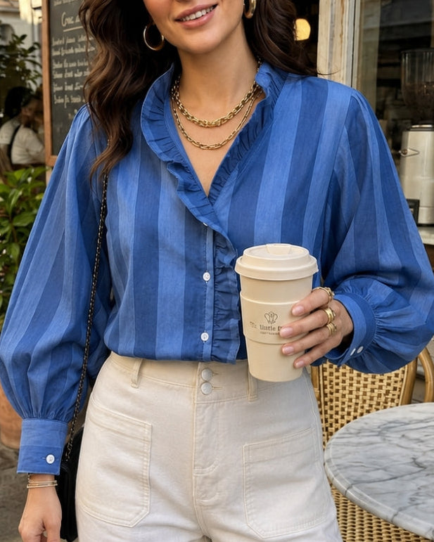 Woman in a blue shirt and white pants holding a coffee cup outside a cafe.