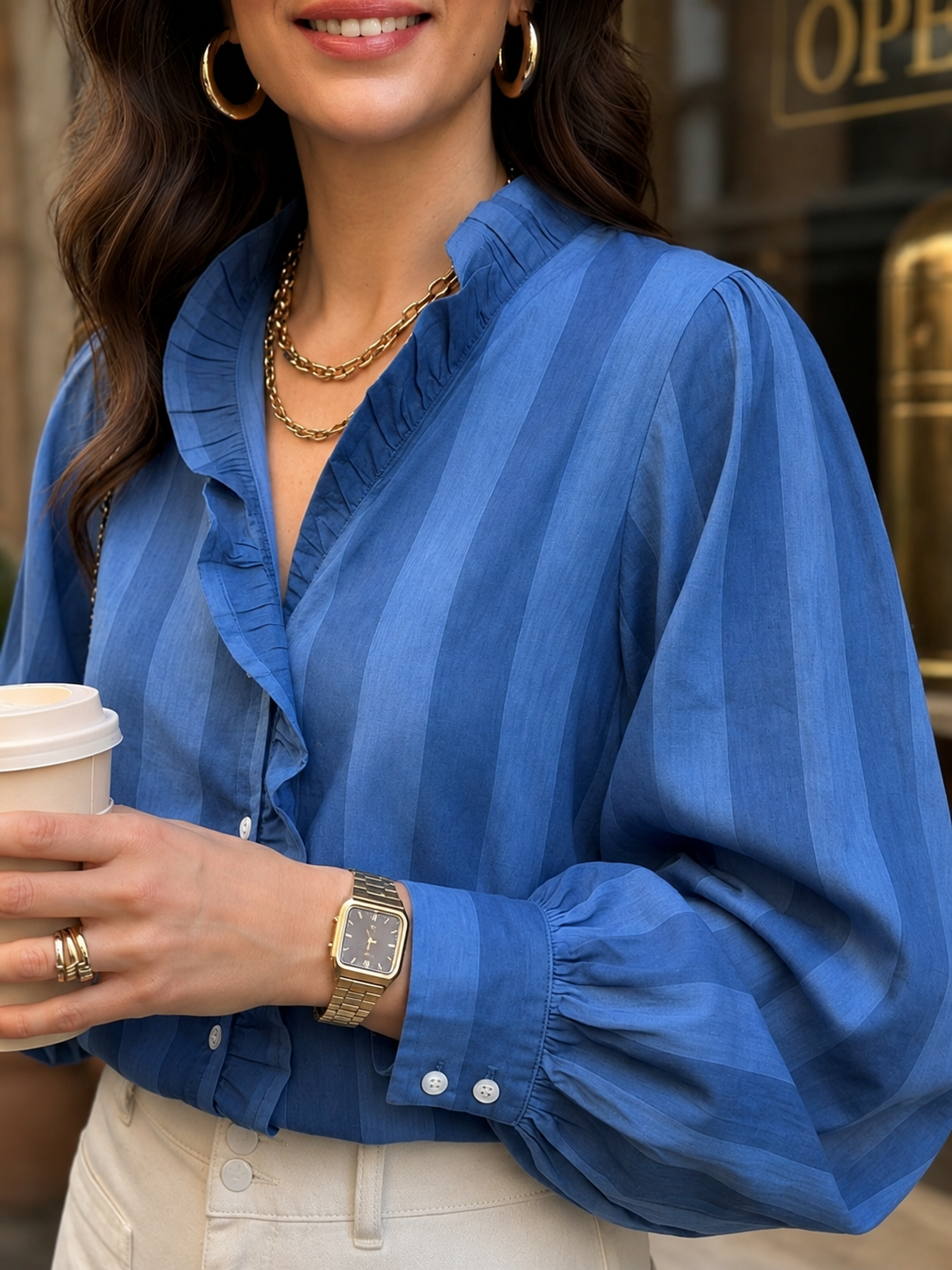 Woman wearing a blue striped shirt, holding a coffee cup, with a blurred background