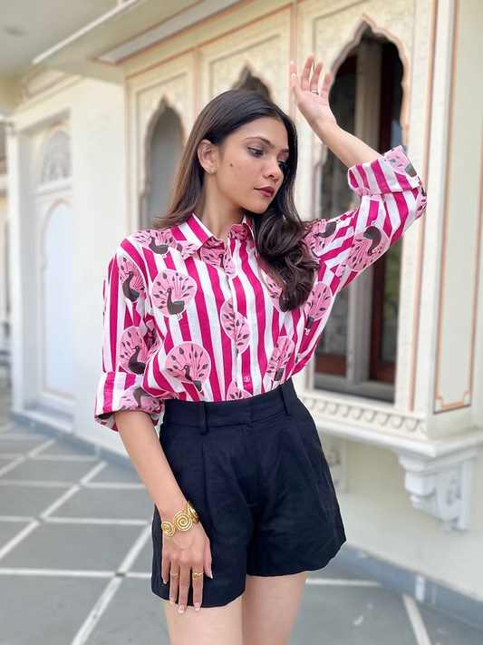 Woman wearing a pink and white striped shirt with black shorts in front of an architectural background.
