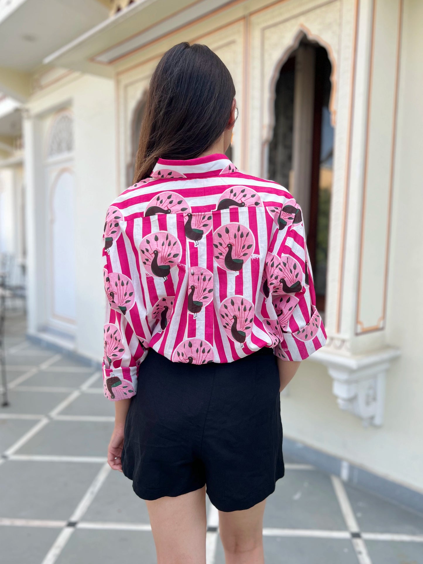 Person wearing a pink and white striped shirt with black patterns, standing in front of a building.