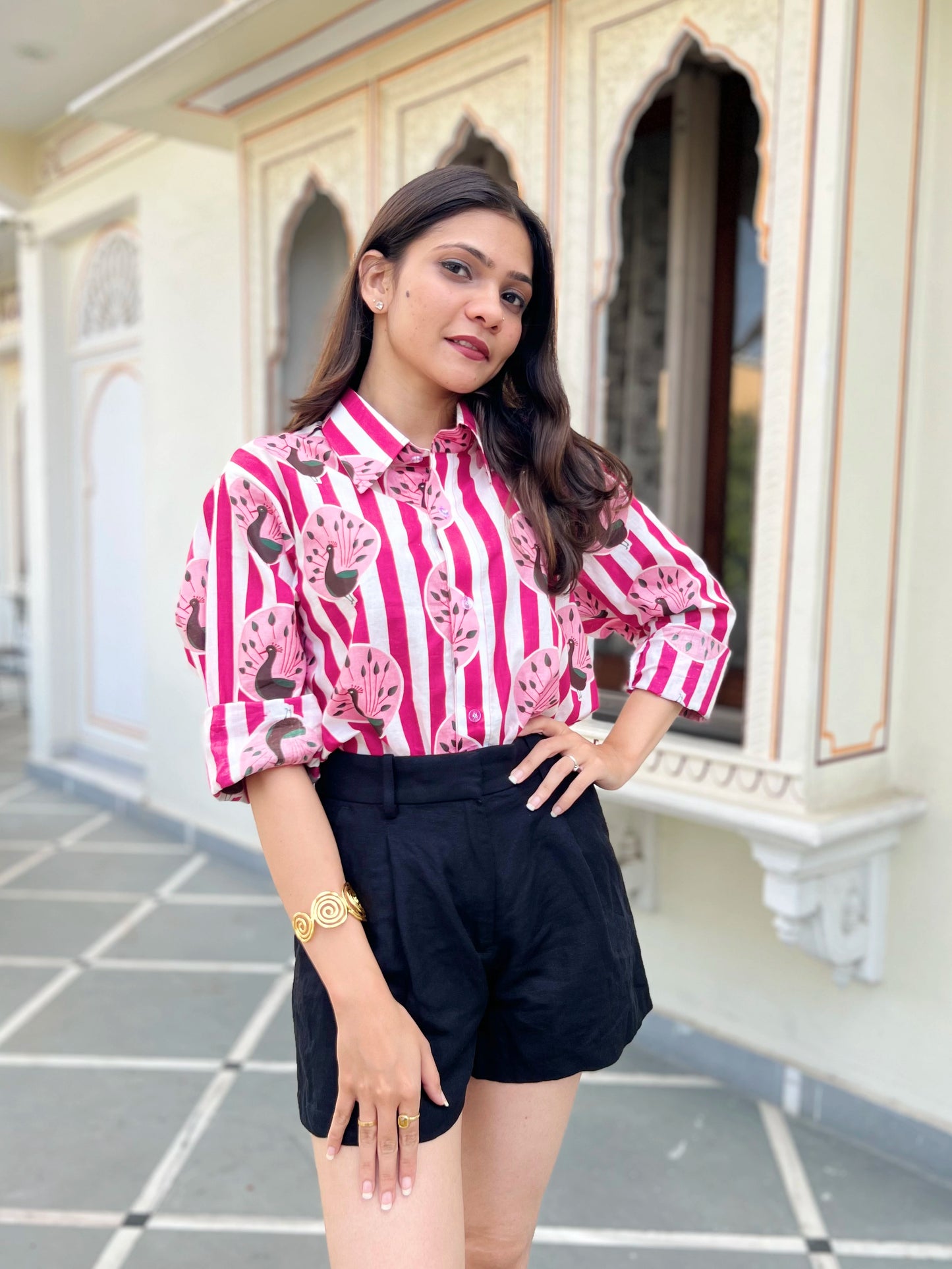 Woman wearing a pink and white striped shirt with black shorts standing in front of an architectural building.