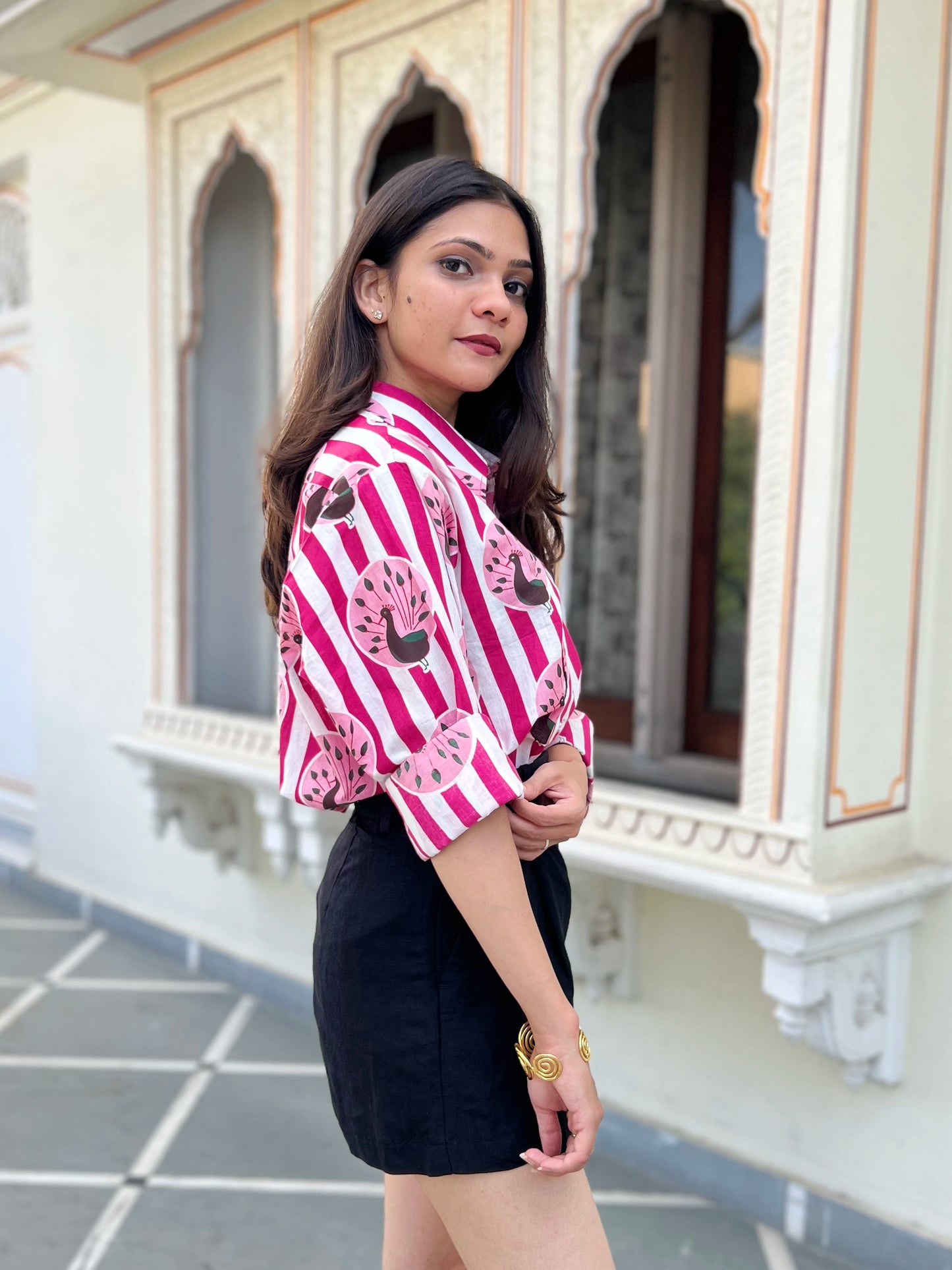 Woman wearing a pink and white striped shirt with black shorts standing in front of an ornate building.
