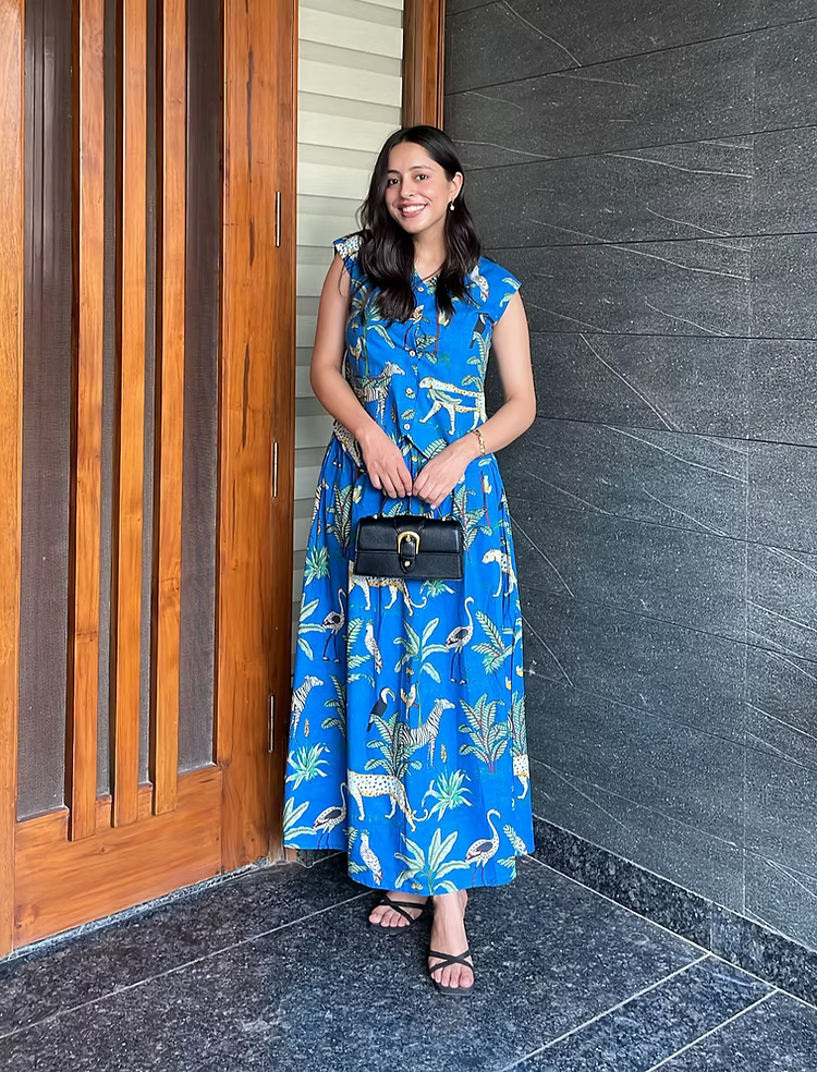 Woman in a blue dress with animal prints standing against a dark wall.