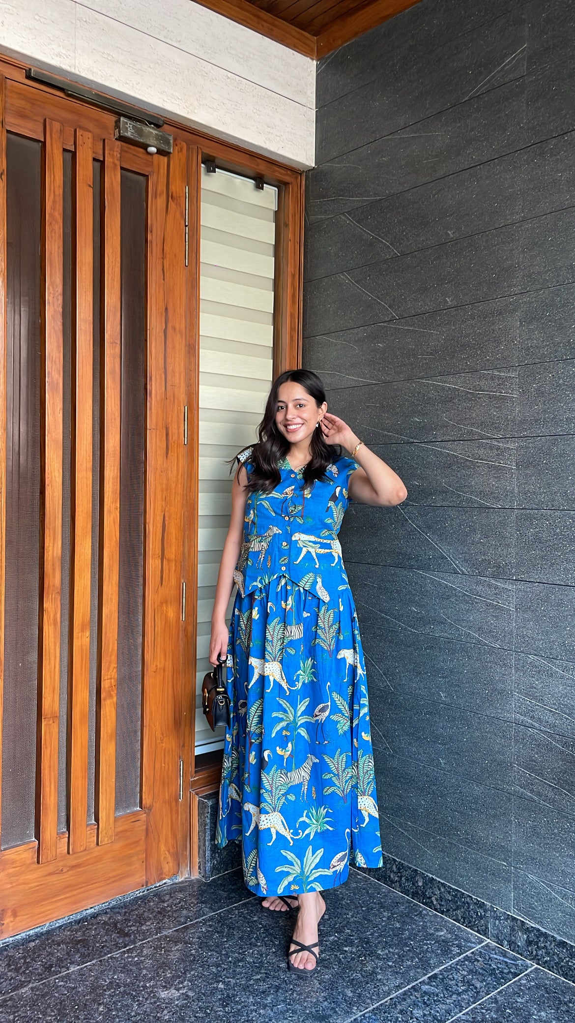 Woman in a blue dress standing in front of a wooden door and gray wall.