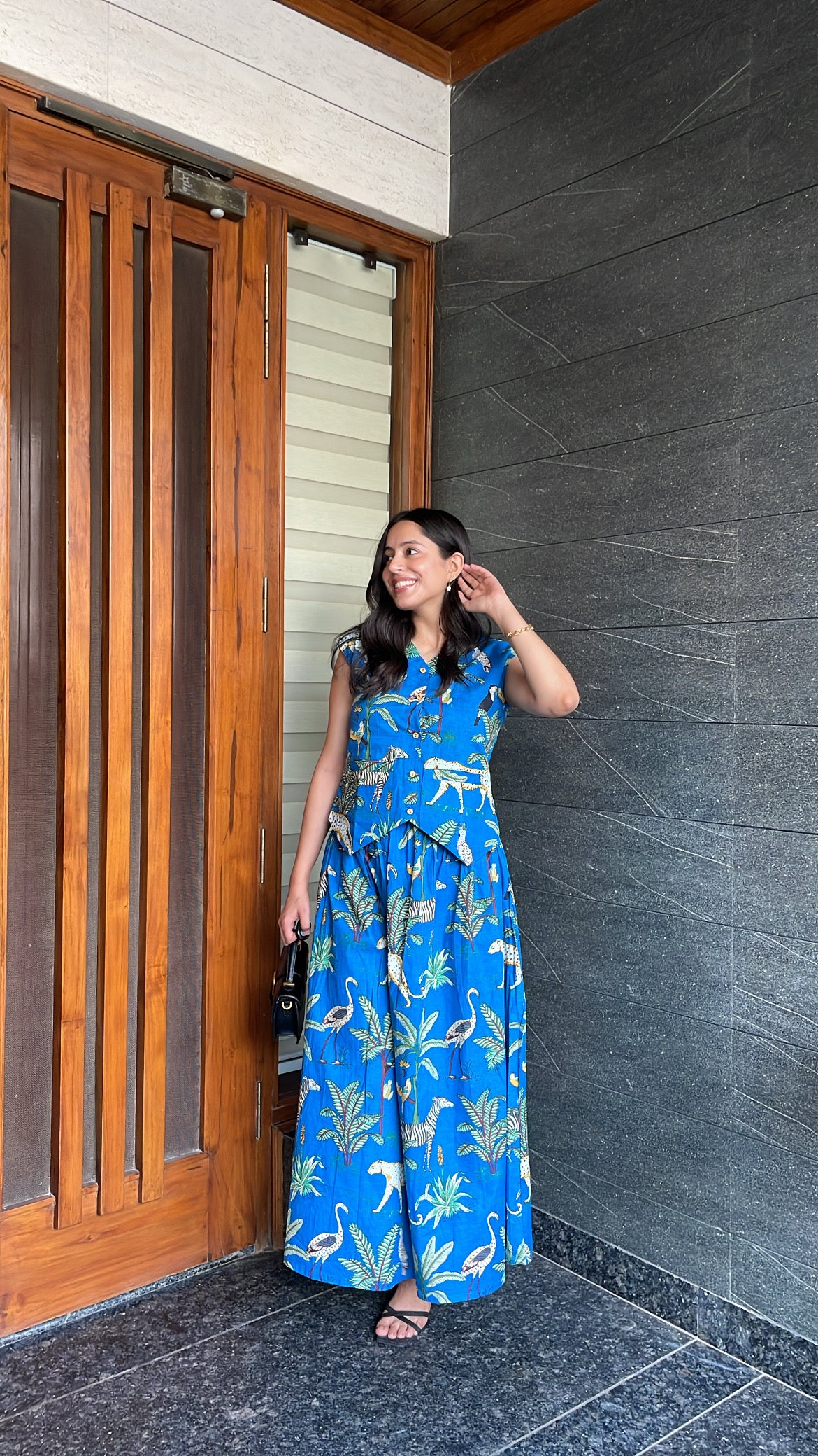 Woman in a blue dress standing in front of a wooden door and gray wall.