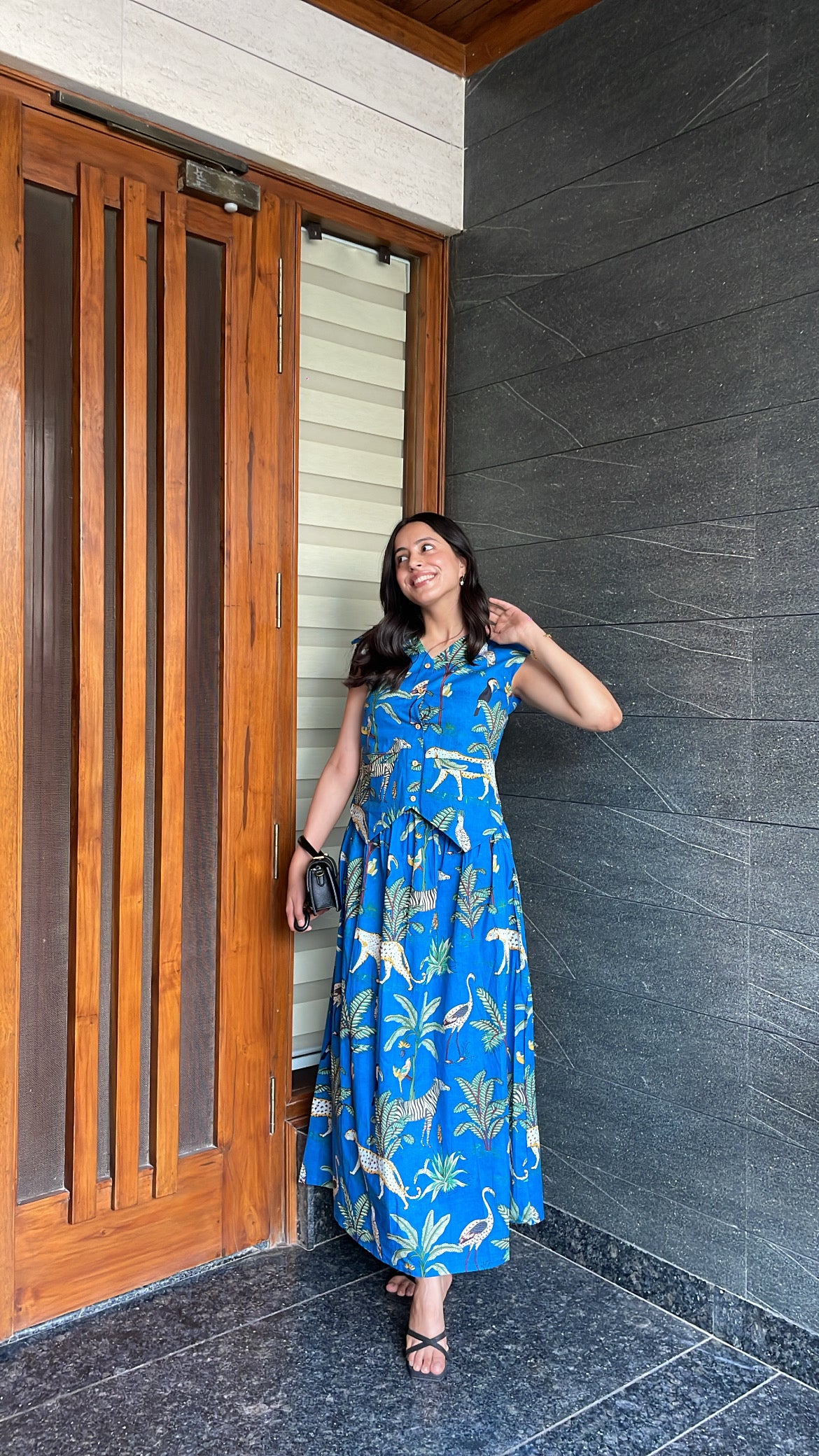 Woman in a blue dress with animal patterns standing next to a wooden door.