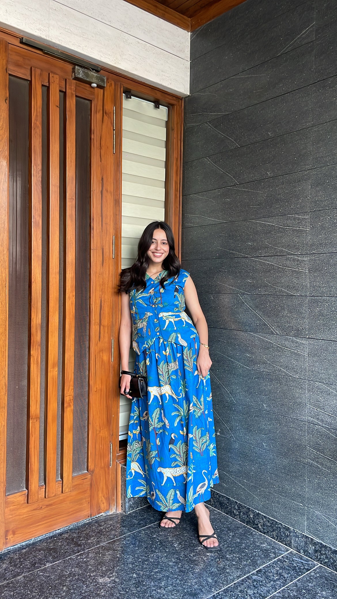 Woman in a blue dress standing in front of a wooden door and gray wall.