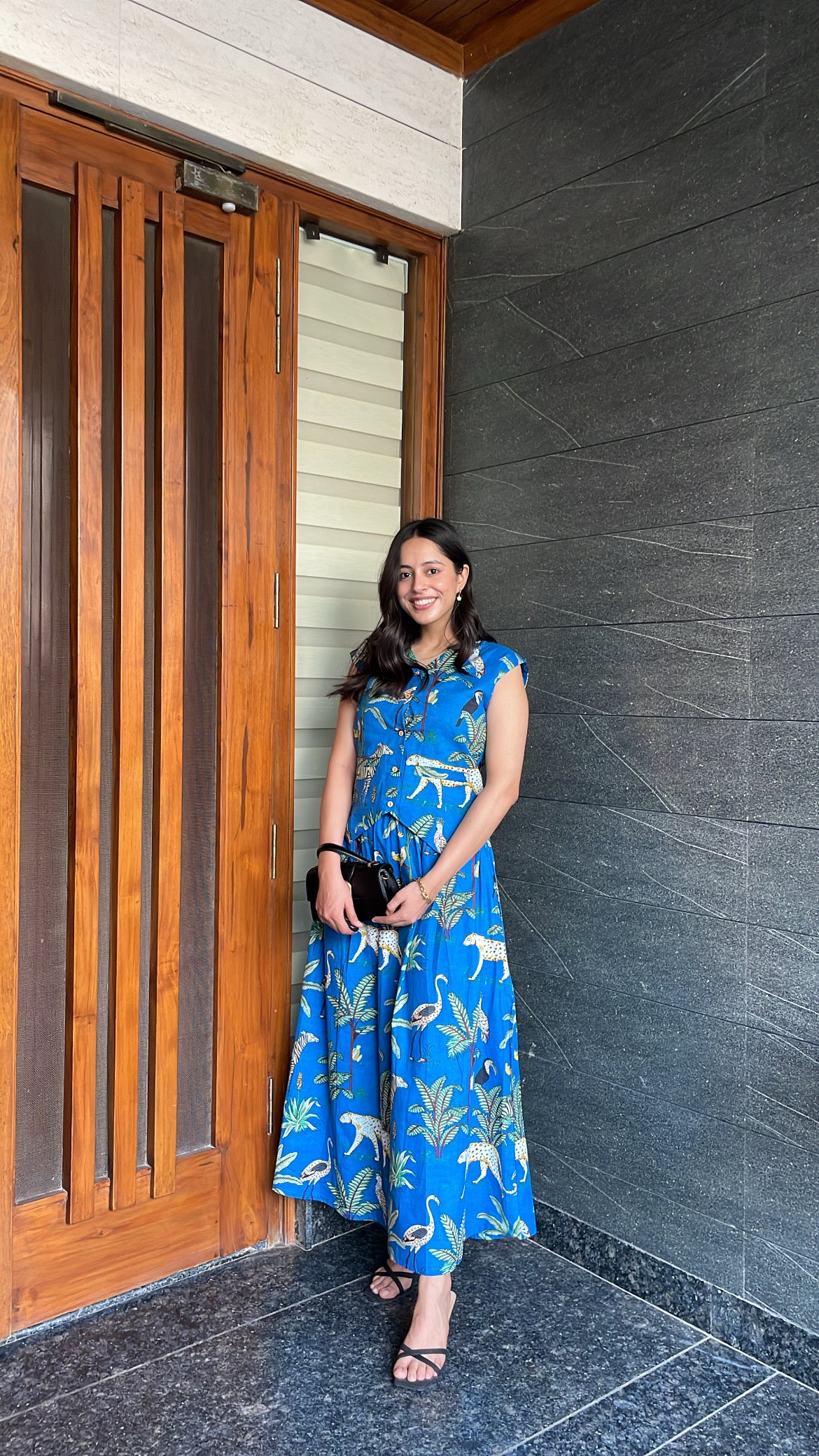 Woman in a blue dress standing next to a wooden door and gray wall.
