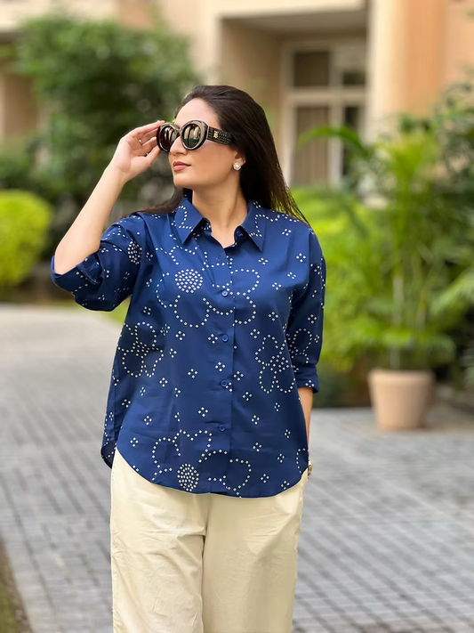 Woman wearing a blue patterned shirt and beige pants outdoors.