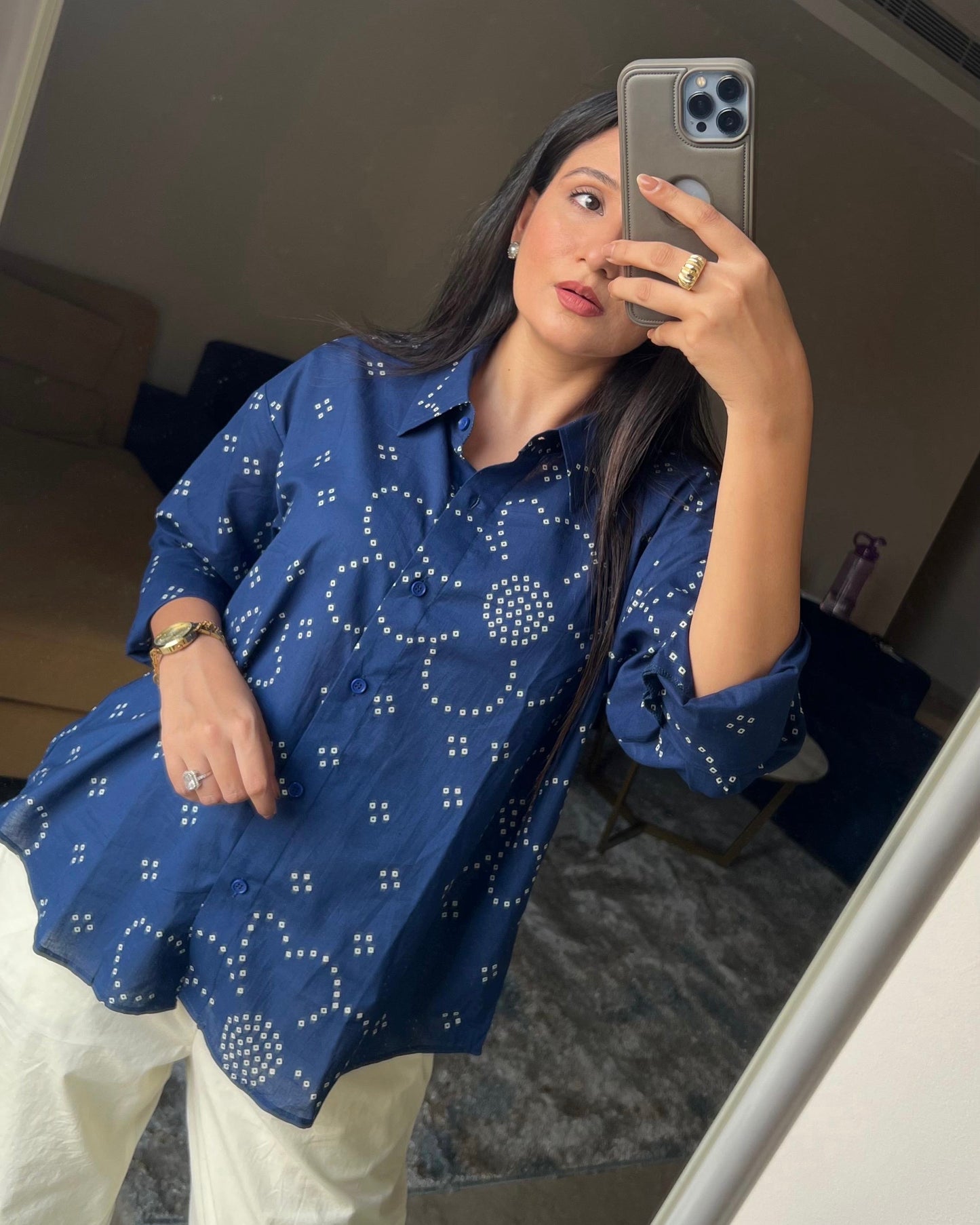 Person wearing a blue patterned shirt taking a mirror selfie.