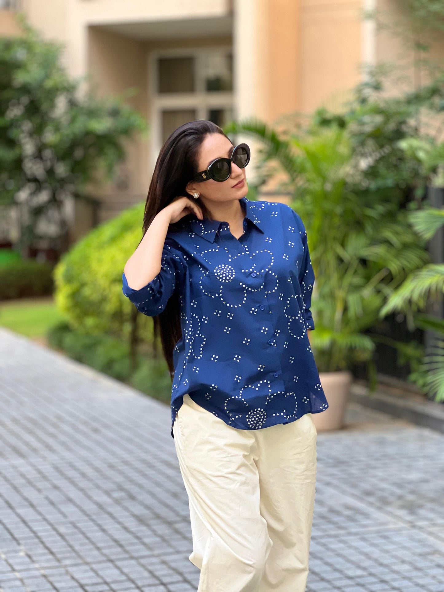 Woman wearing a blue patterned shirt and beige pants outdoors.