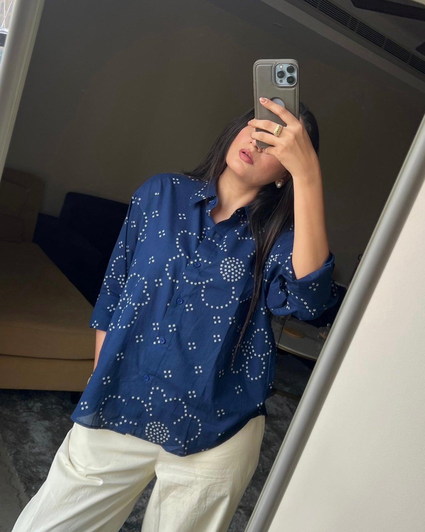 Person wearing a blue patterned shirt and white pants taking a mirror selfie.