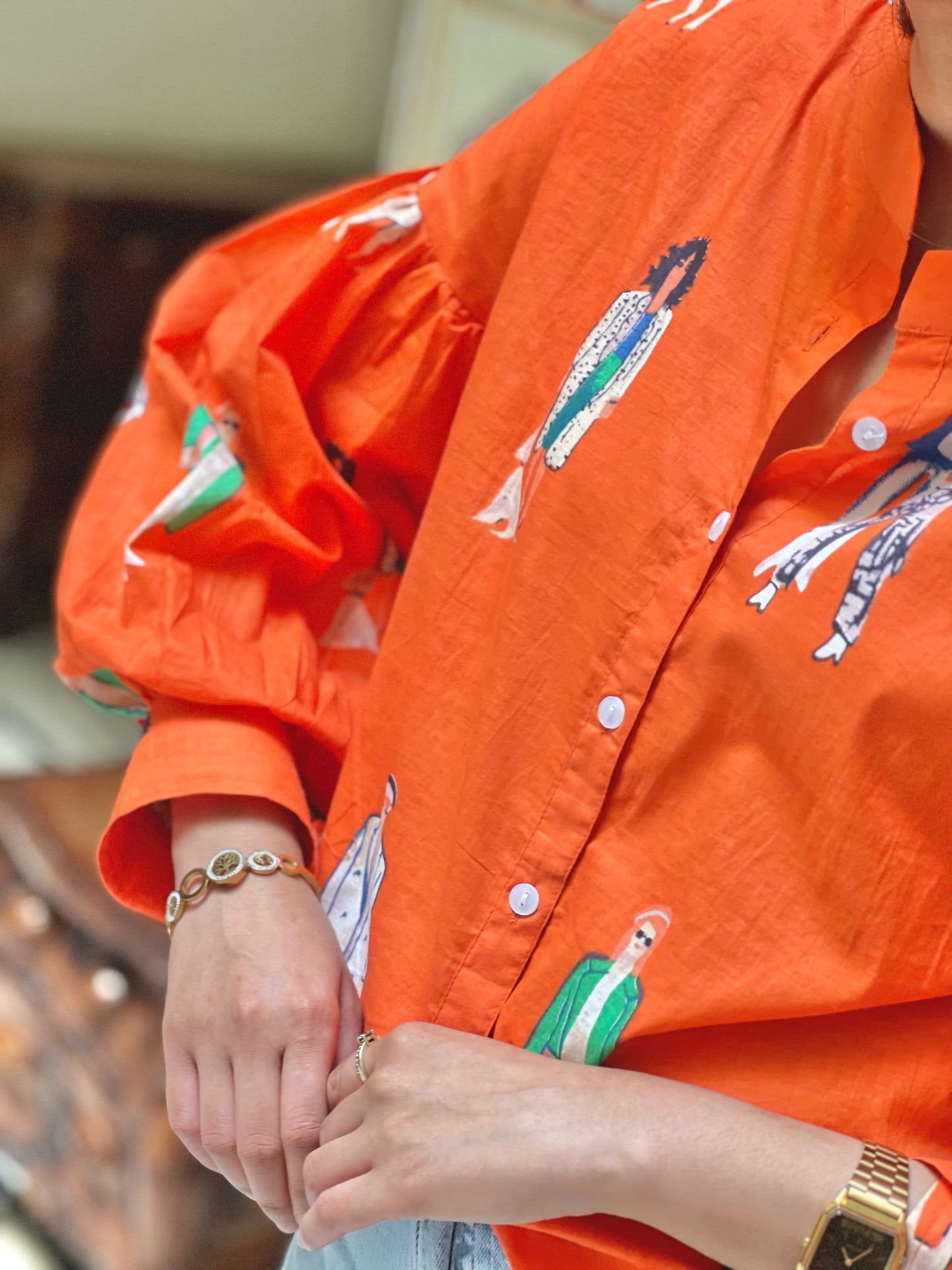 Person wearing an orange shirt with graphic designs, holding hands with another person.