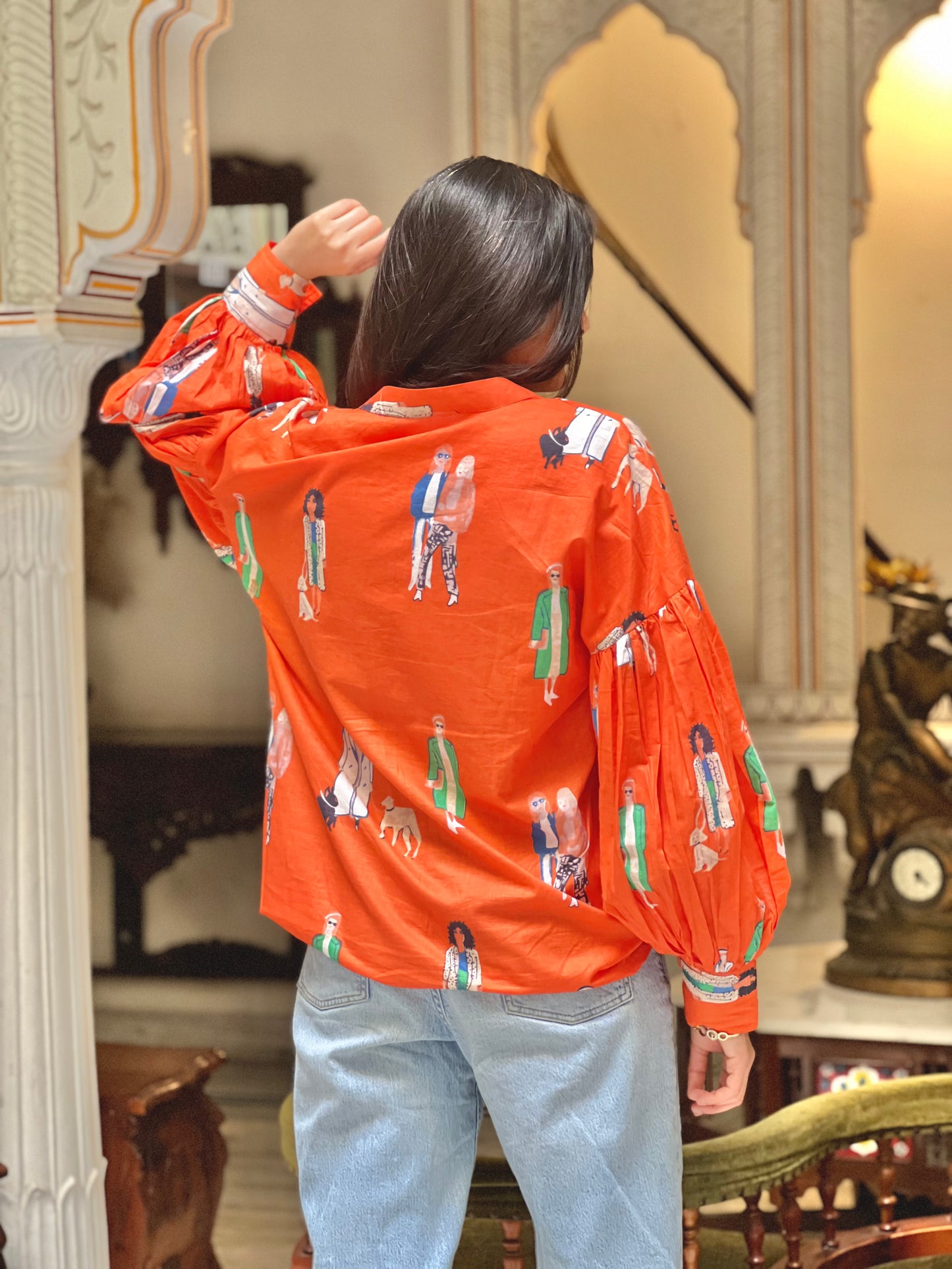 Person wearing an orange jacket with graphic designs in a decorative interior setting