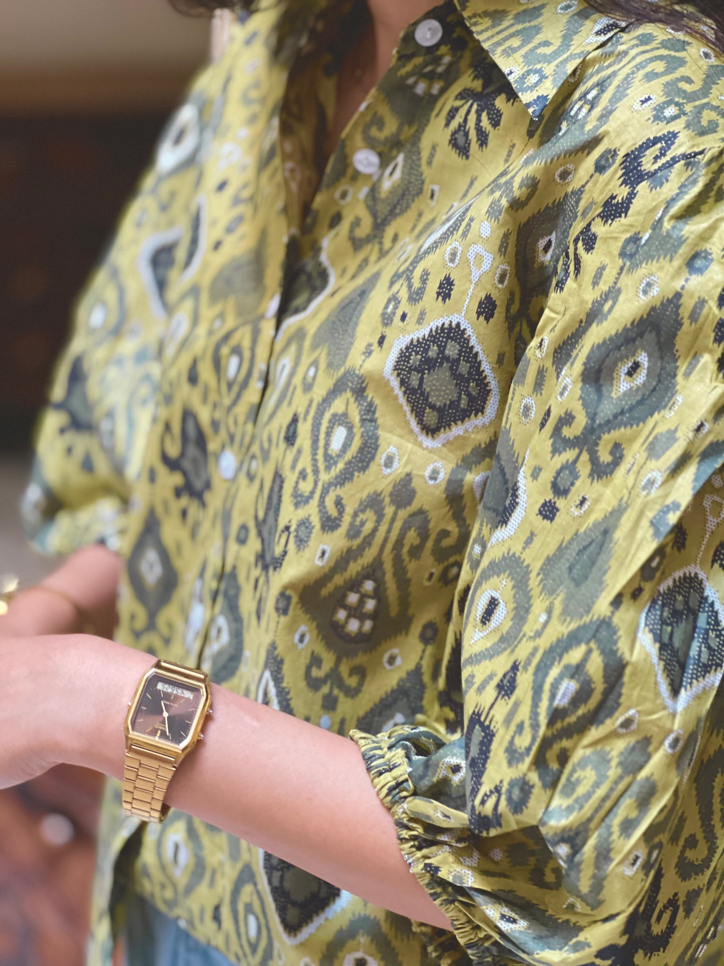 Person wearing a yellow patterned shirt with a gold watch on wrist