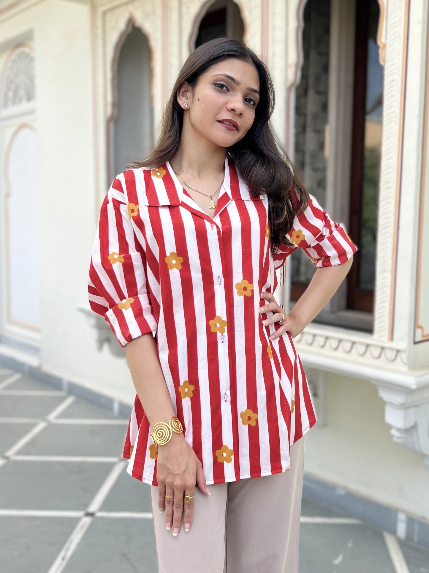 Woman wearing a red and white striped shirt with floral patterns, standing in front of an architectural background.