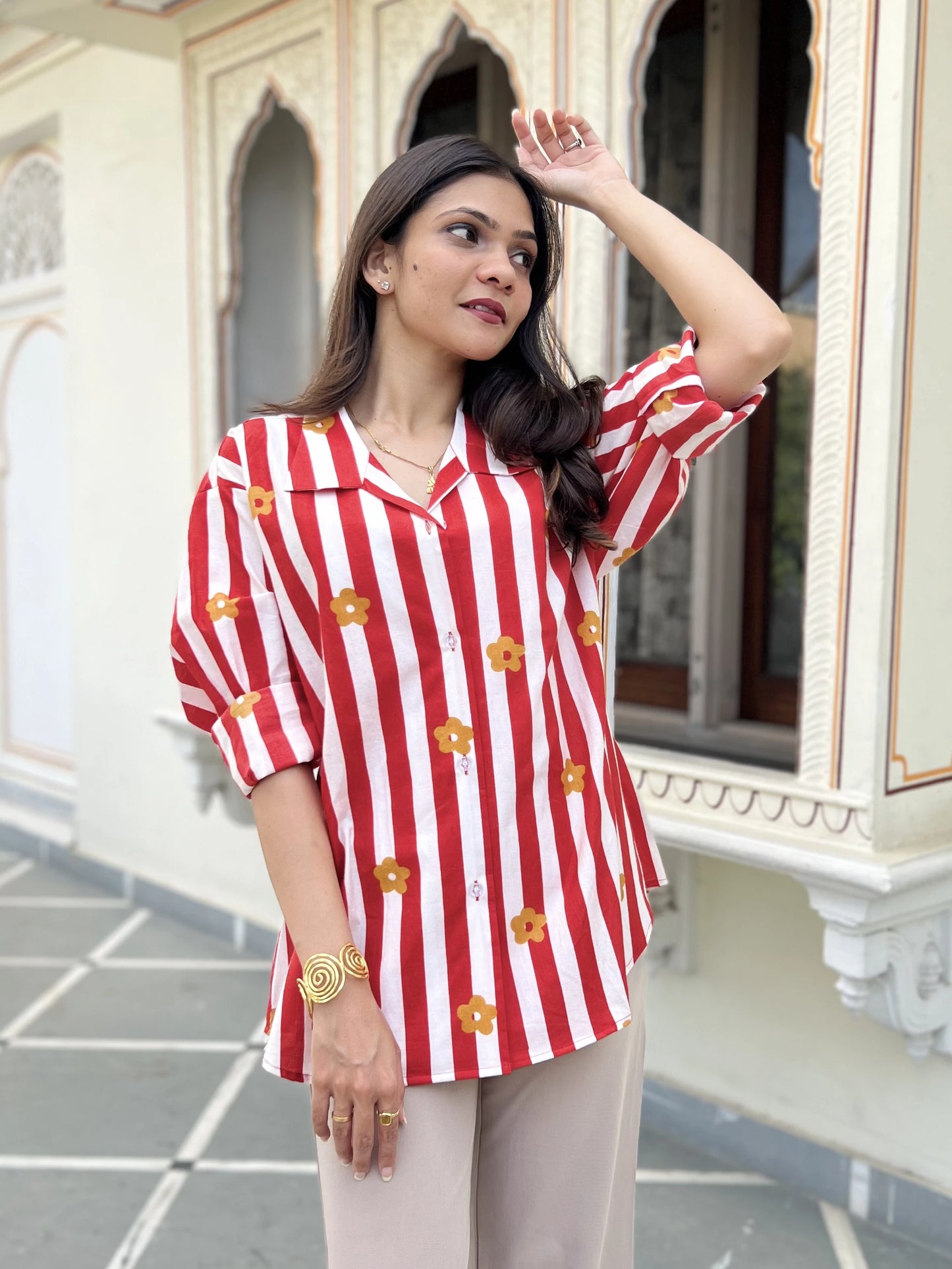 Woman wearing a red and white striped shirt with floral patterns in an outdoor setting.
