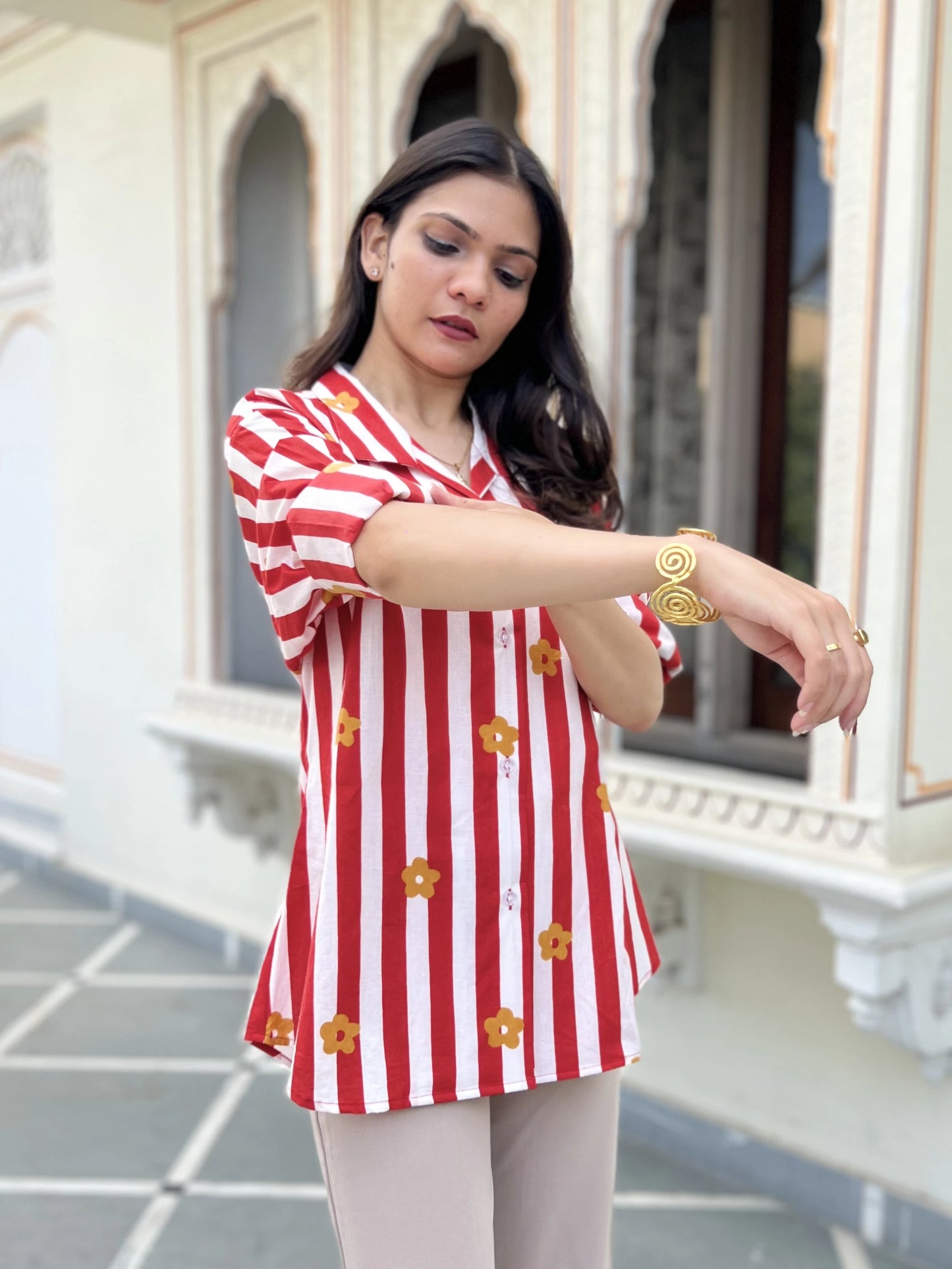 Woman wearing a red and white striped shirt with yellow flowers, standing in front of an architectural background.