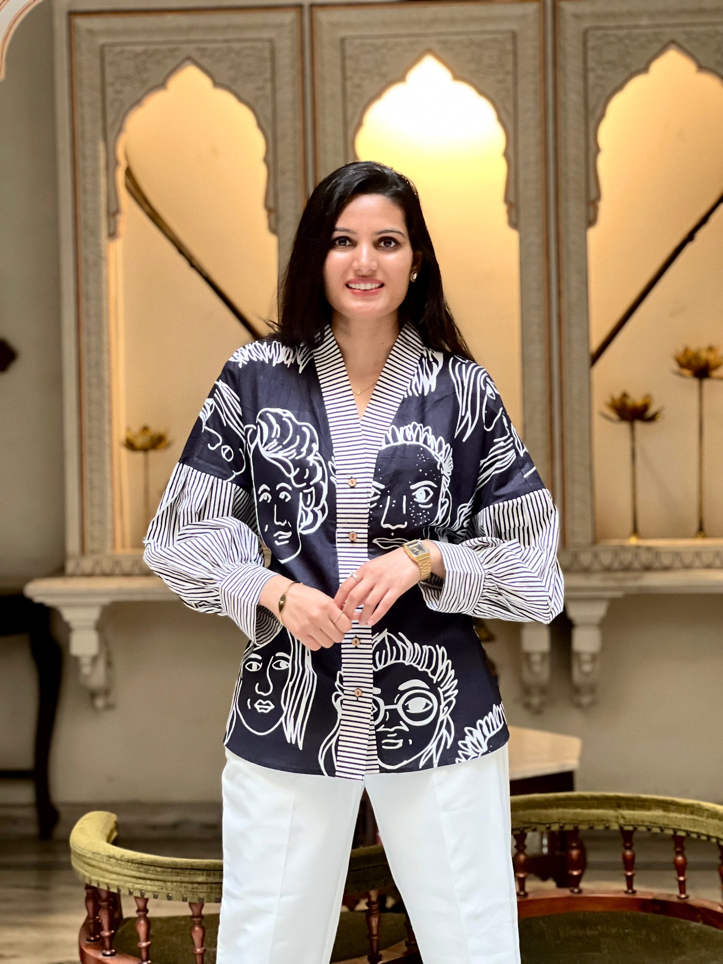 Woman wearing a patterned shirt and white pants in an ornate room.