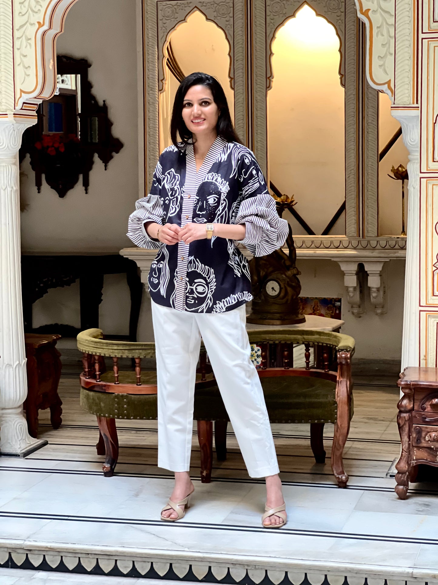 Woman in a patterned top and white pants standing in an ornate room.