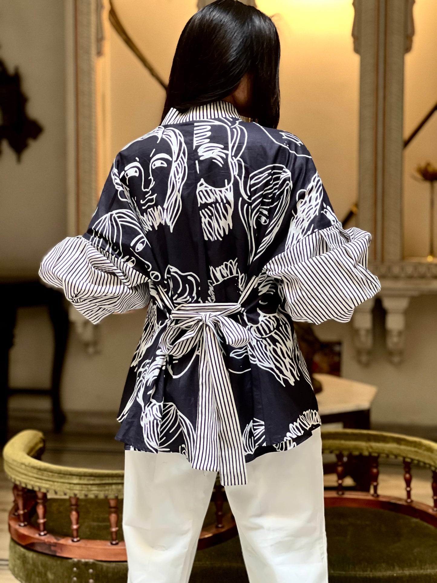 Person wearing a black and white patterned kimono-style top with long sleeves in an indoor setting.