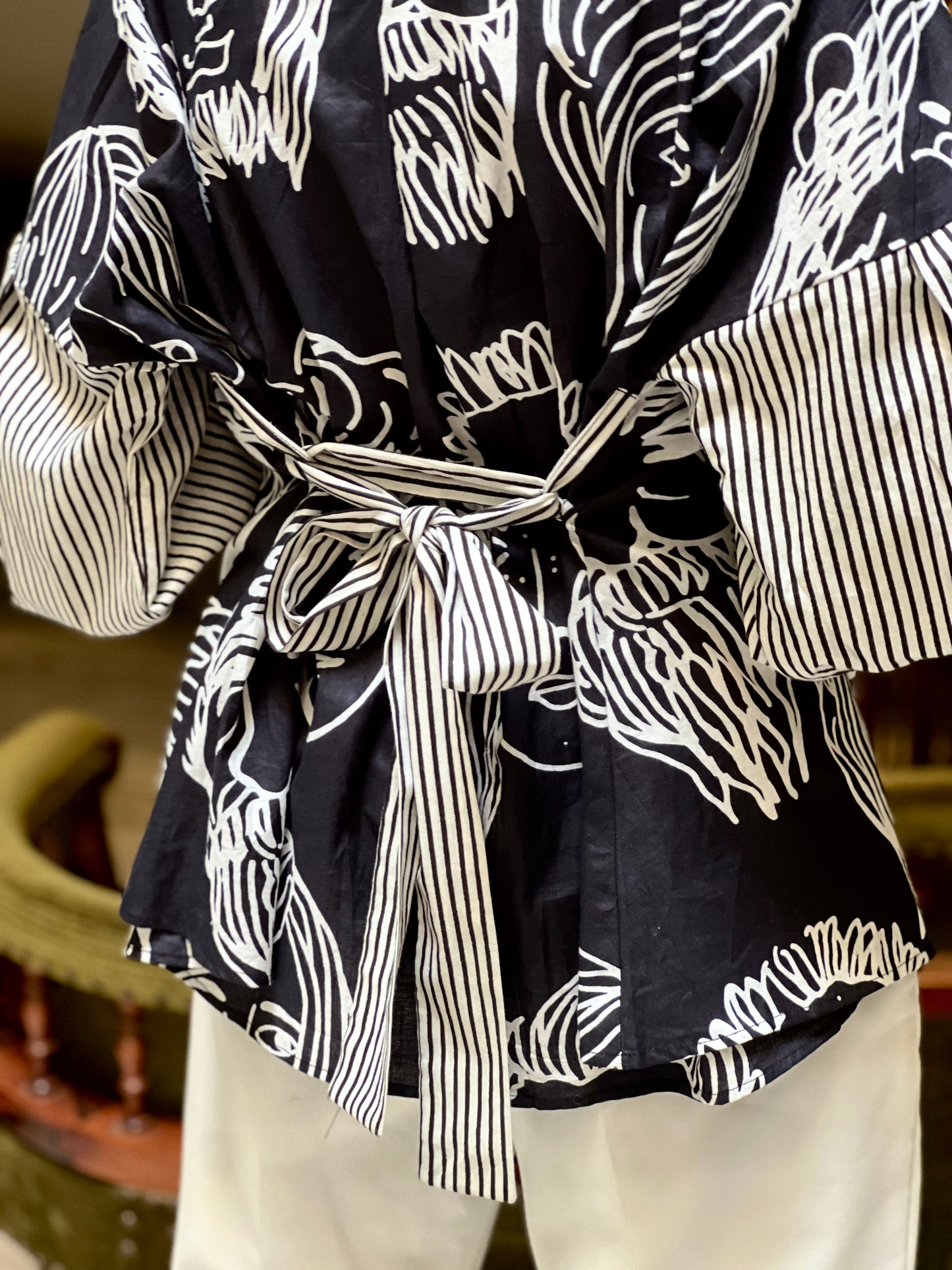 Black and white patterned dress with a tie waist, worn over light-colored pants.