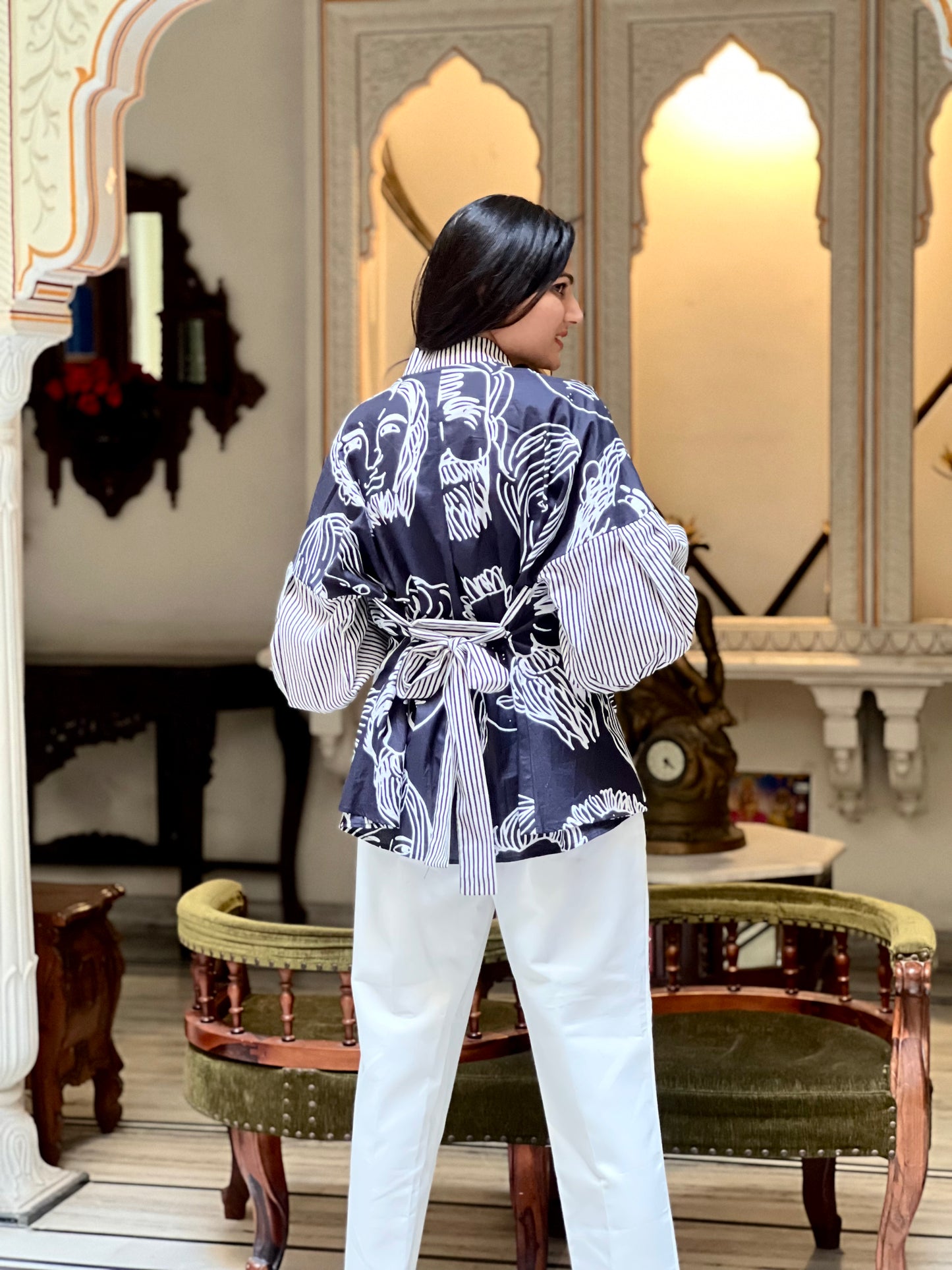 Person wearing a patterned outfit in an ornate room with mirrors and furniture.