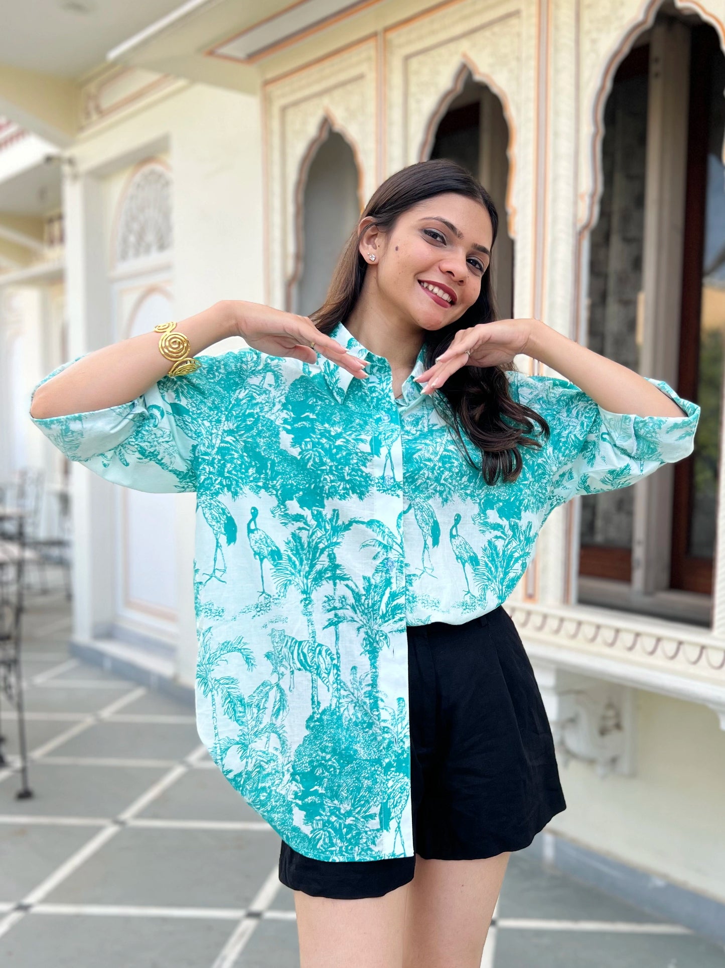 Woman wearing a turquoise floral blouse and black shorts in an outdoor setting.