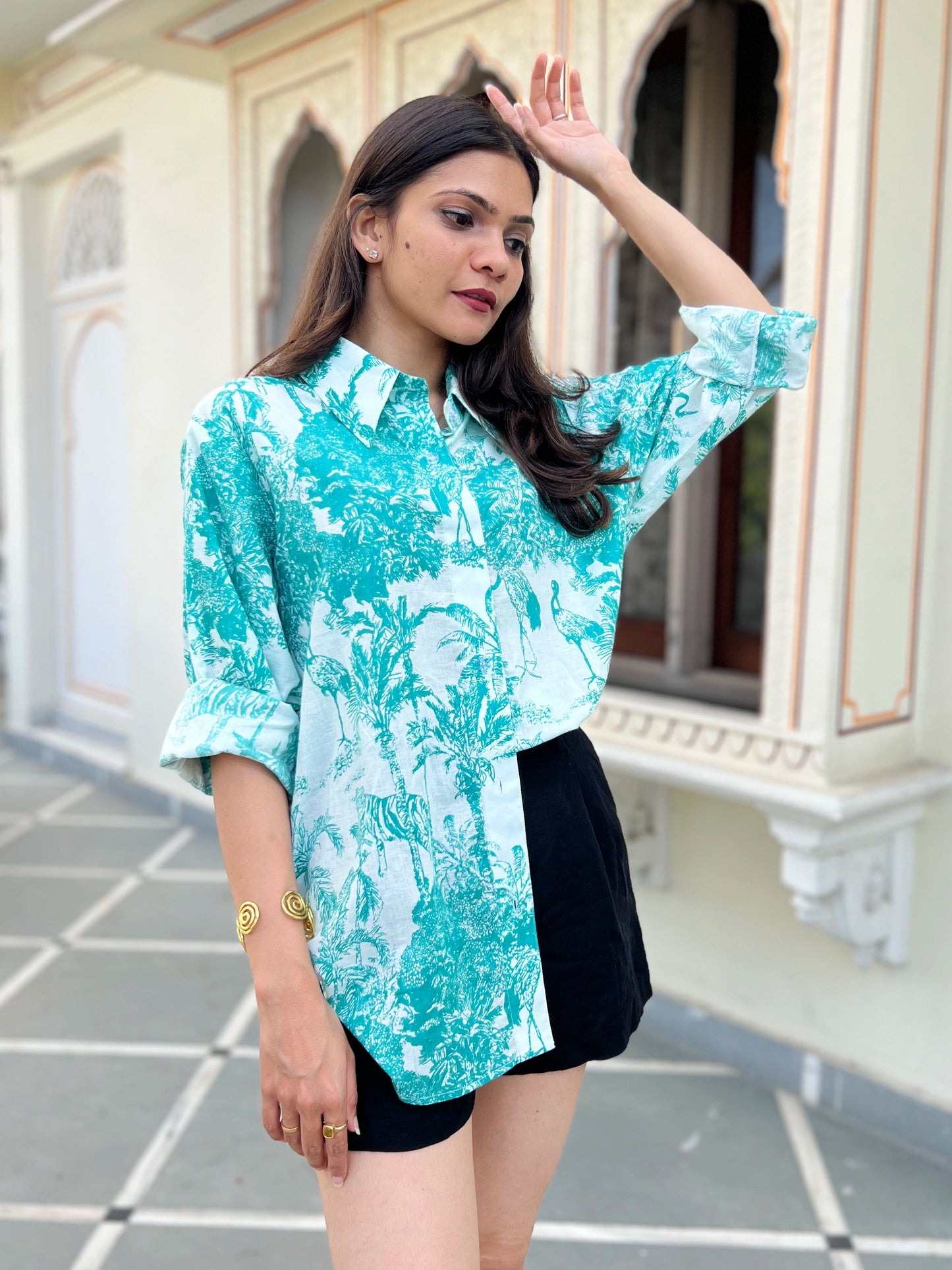 Woman wearing a turquoise floral blouse and black shorts standing in front of an architectural building.
