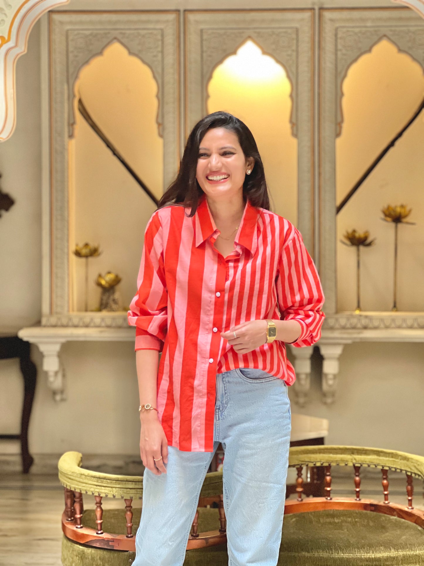 Woman wearing a red and white striped shirt and light blue jeans standing in a decorative interior setting.