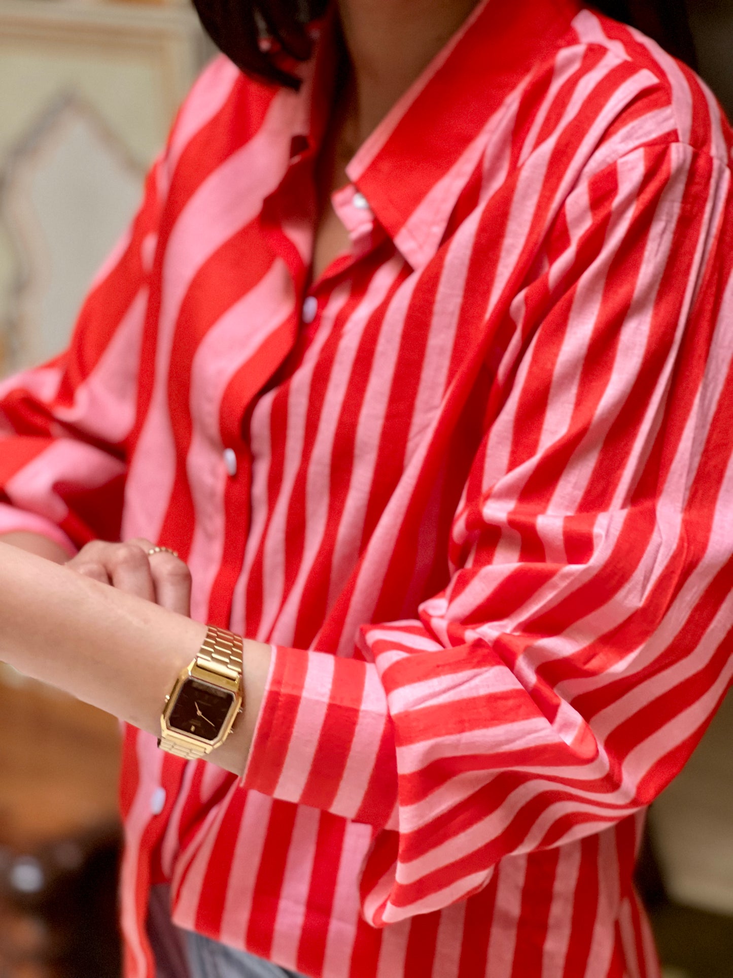 Person wearing a red and white striped shirt with a gold watch on a blurred background
