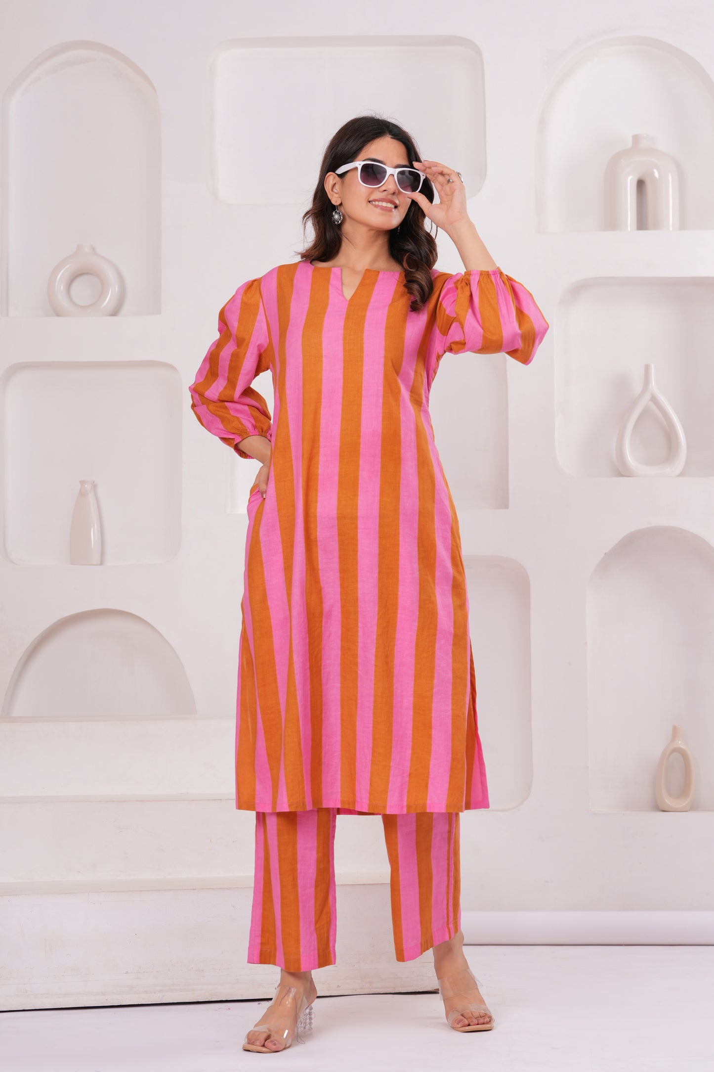 Woman wearing a pink and orange striped outfit against a white decorative wall.